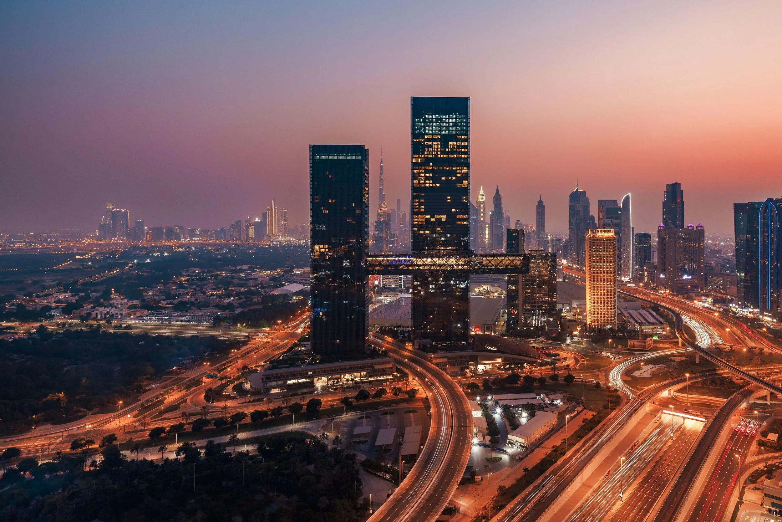 Twilight view of Dubai skyline with tall skyscrapers and illuminated highways.