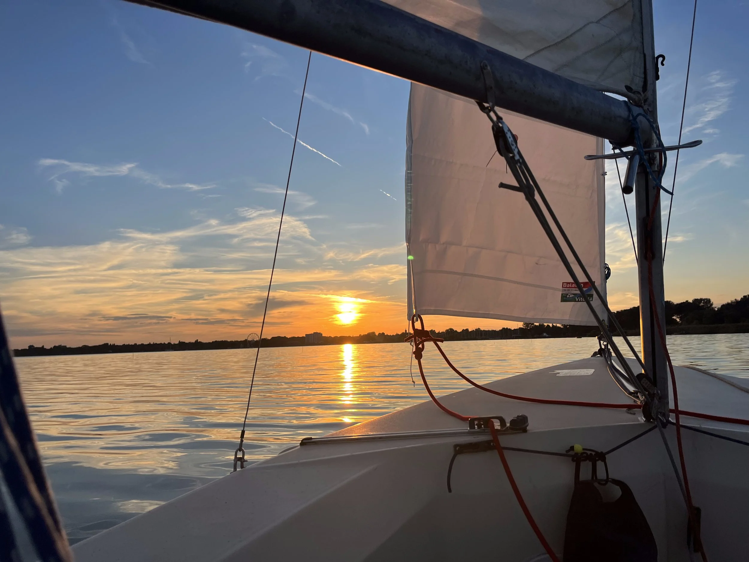 Sailing boat on calm water during sunset or sunrise with a partly cloudy sky.