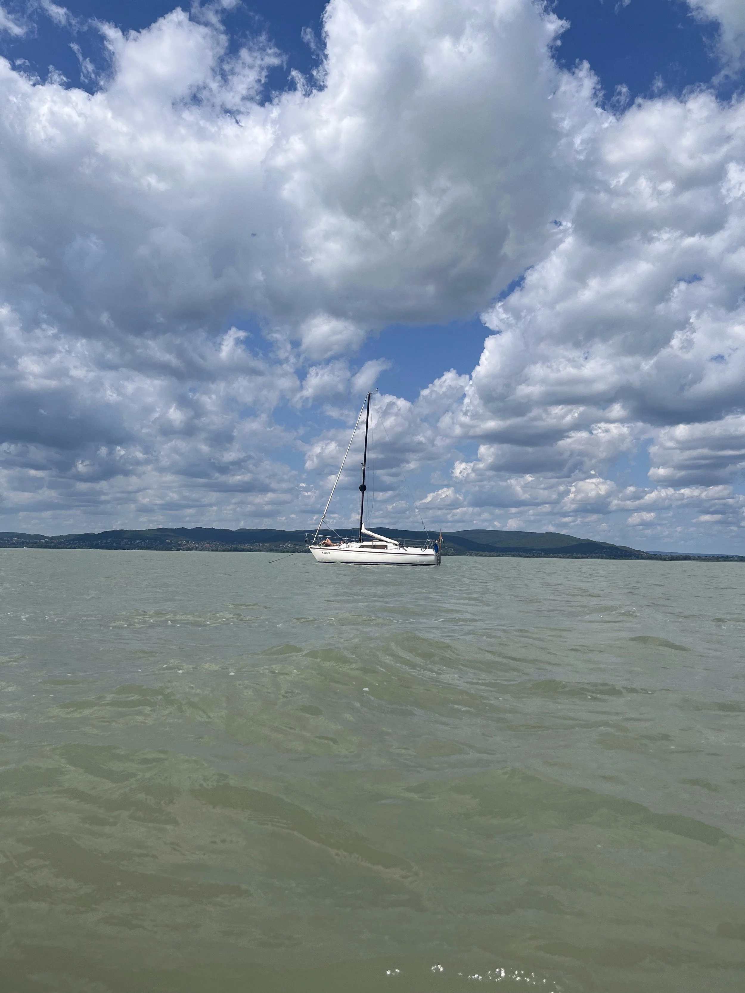 A sailboat floating on a calm body of water with a cloudy sky and mountains in the background.
