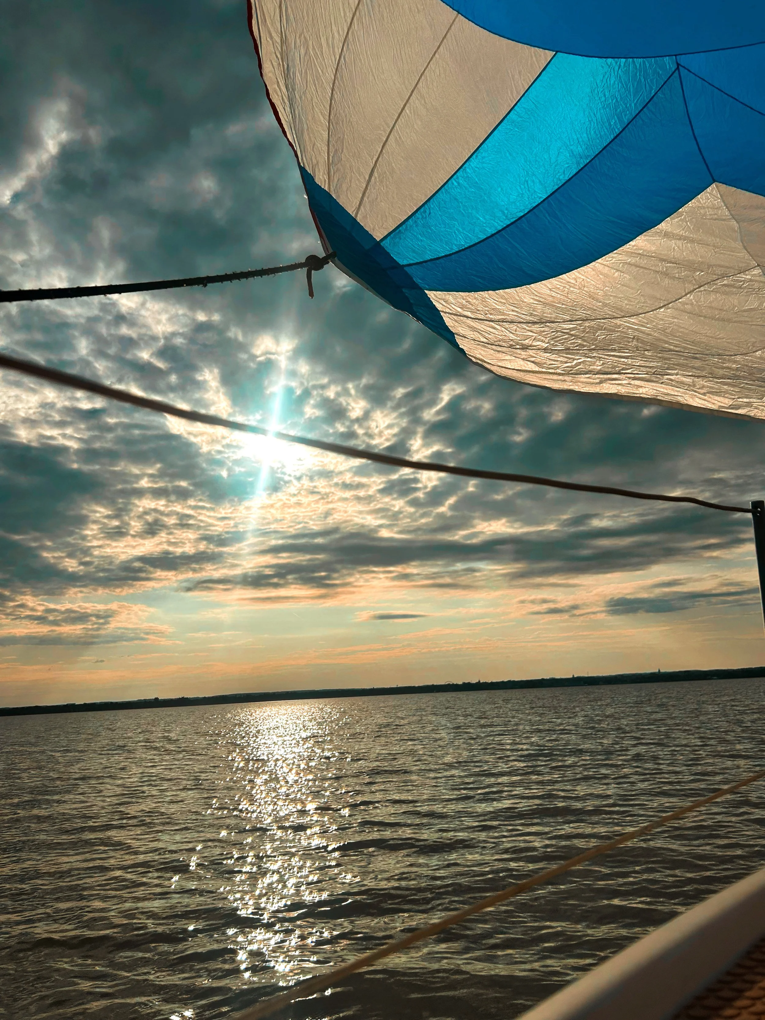 View of a hot air balloon partially visible in the sky over a body of water during sunset or sunrise, with clouds and sun rays reflecting on the water.