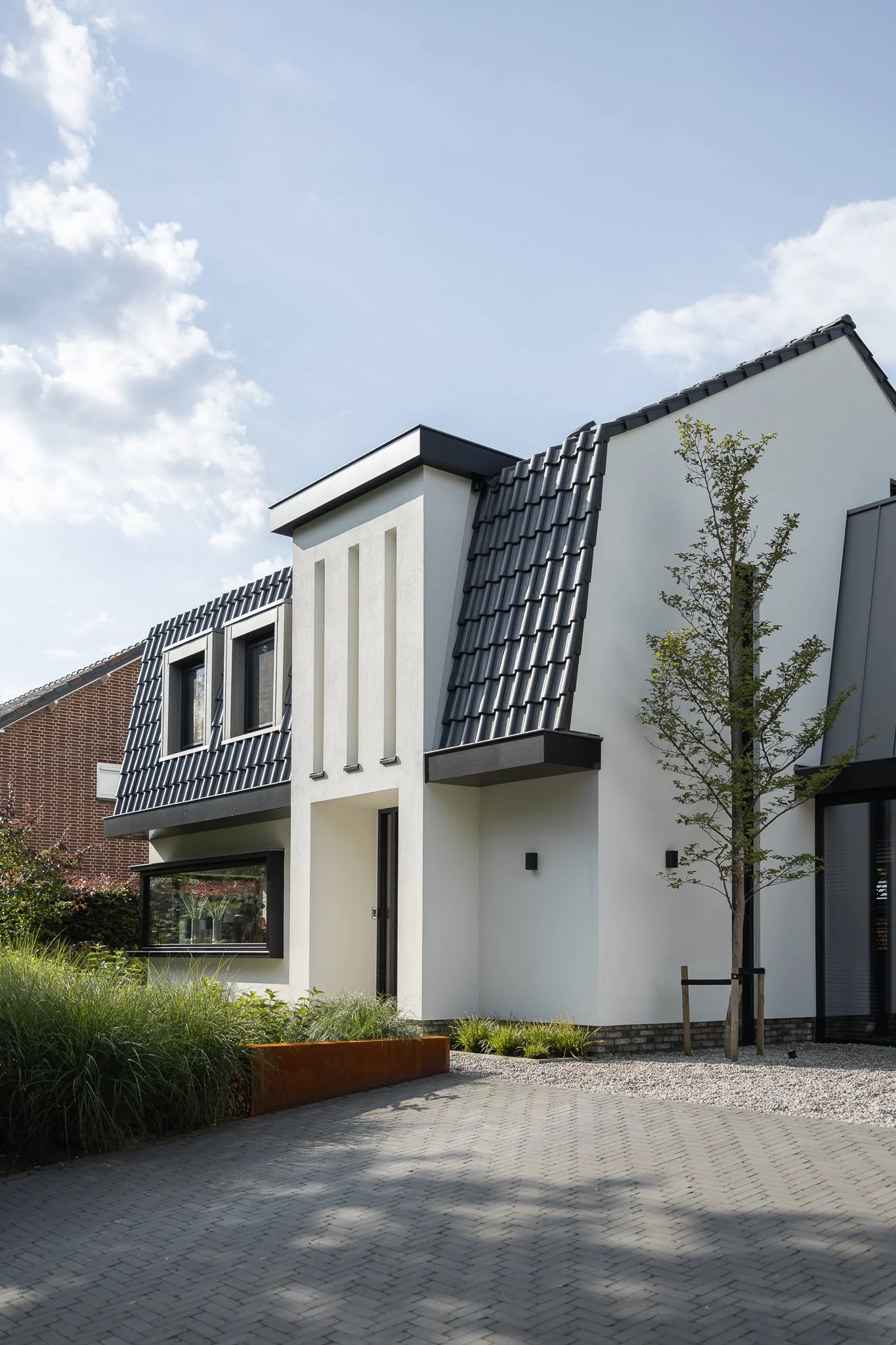 Side elevation of a white villa with dark roof tiles, dormer window and layered planting