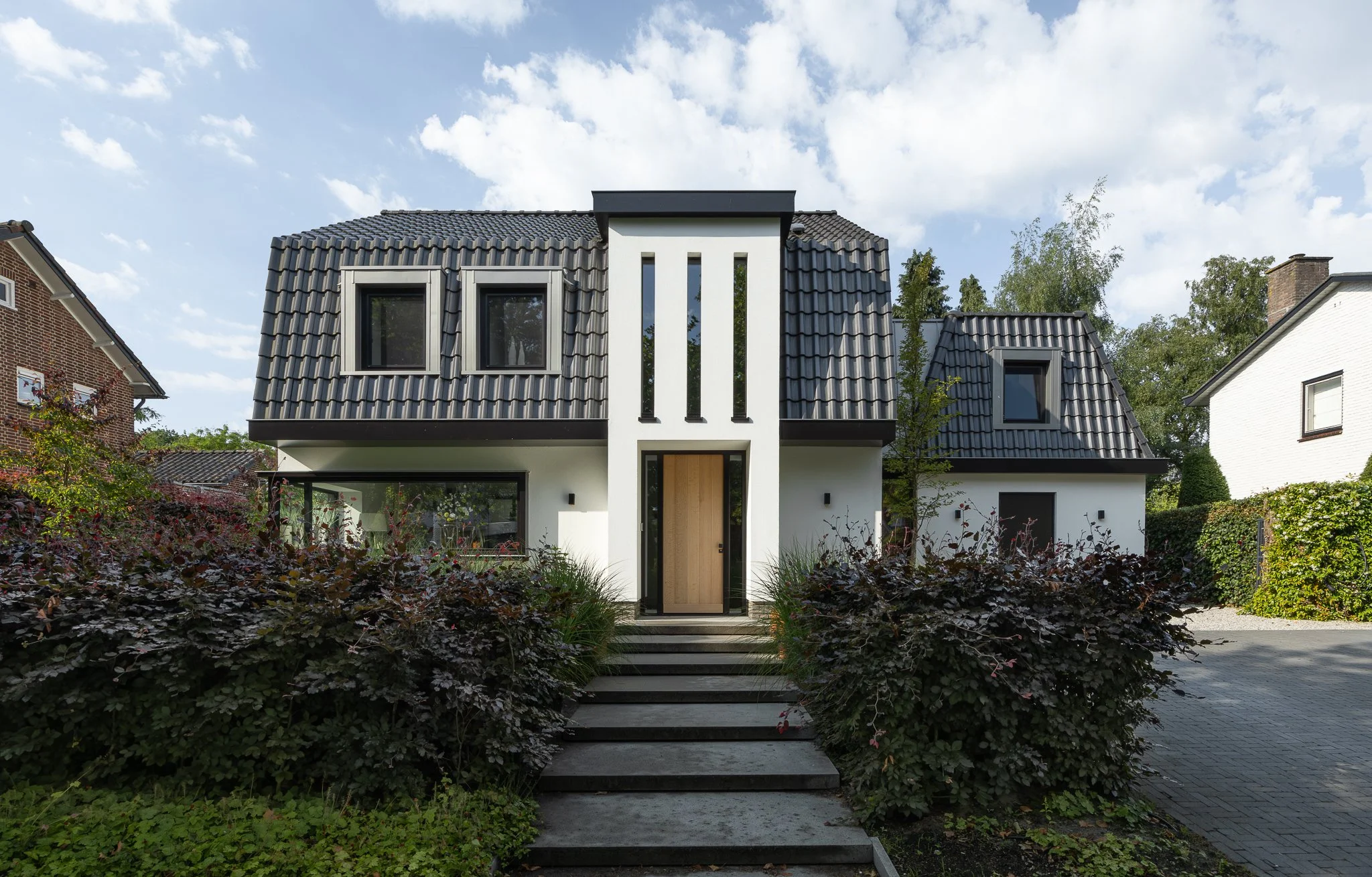 Contemporary white villa with dark tiled roofs, black detailing and a landscaped front garden