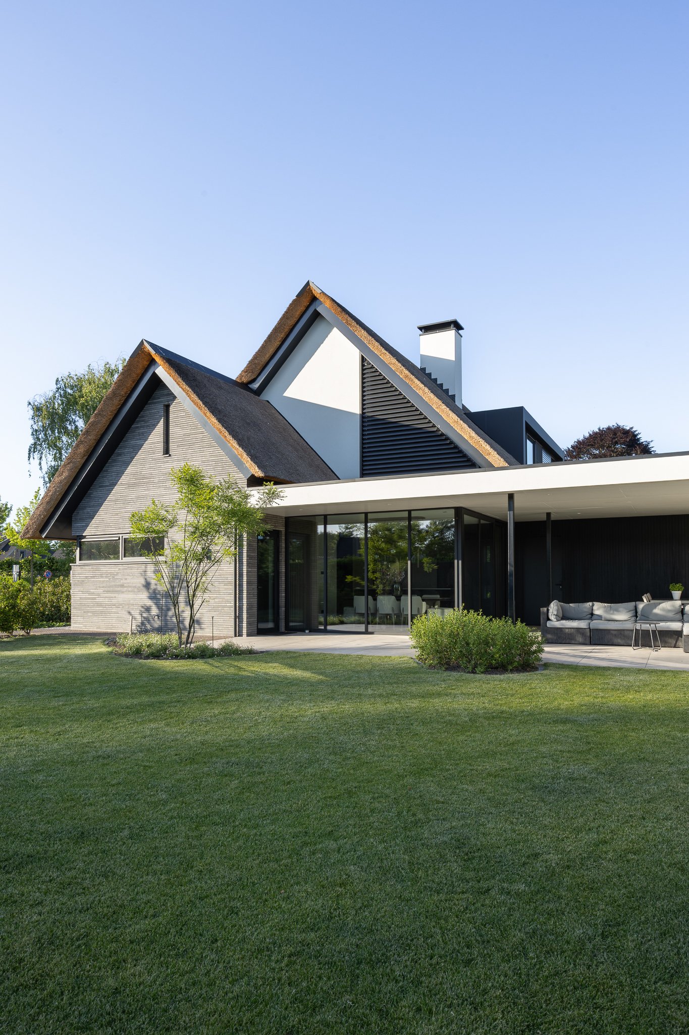 Modern villa with a thatched roof, tall windows and landscaped greenery in warm sunlight