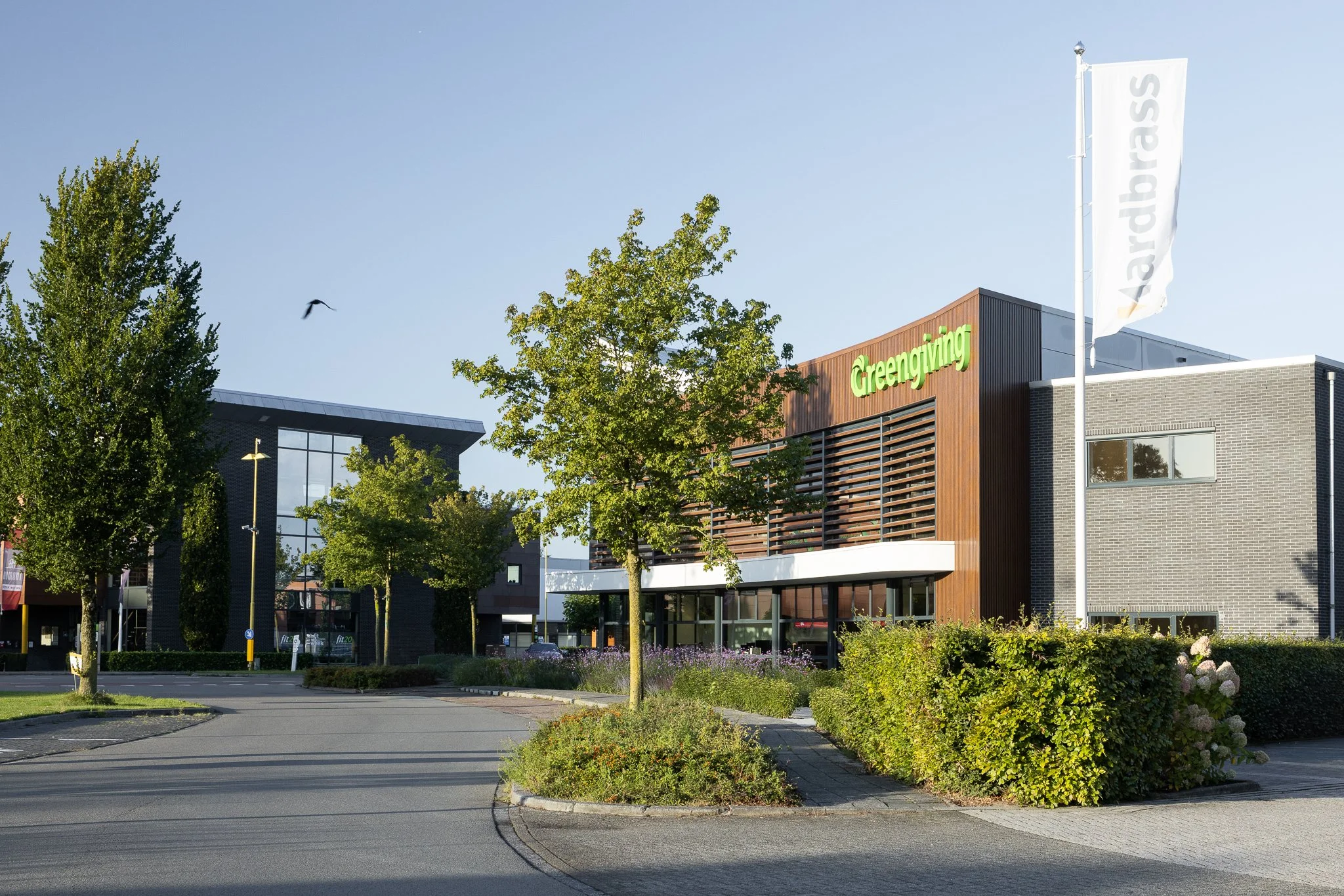 Modern office façade with curved white canopy, wooden slats and flowering landscaping