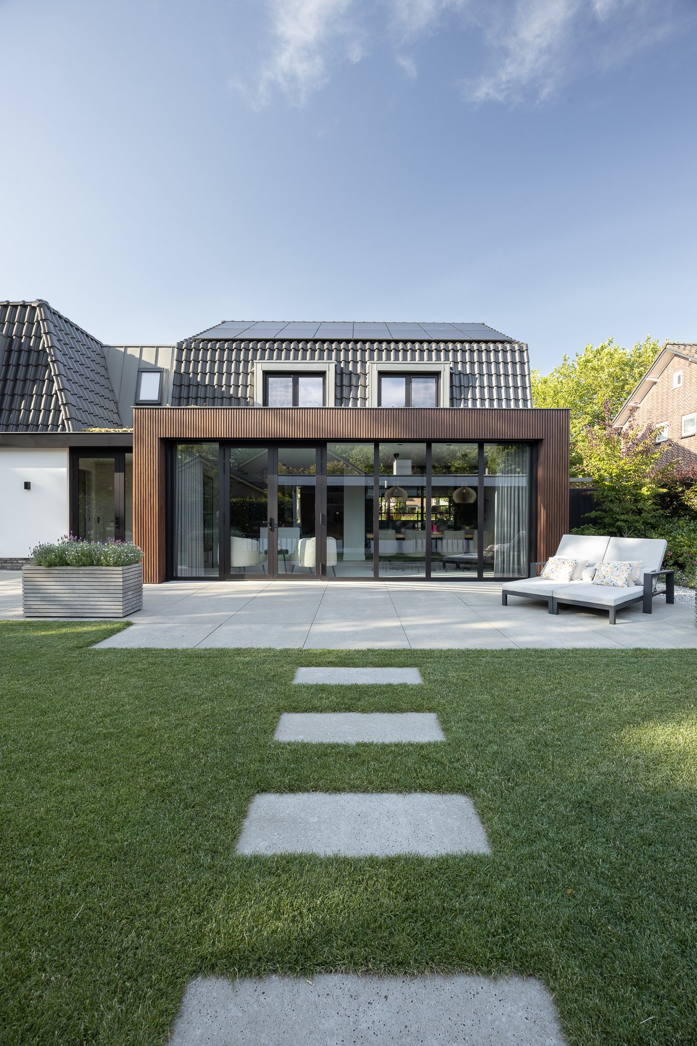Modern timber-clad extension viewed across a green lawn with concrete stepping stones