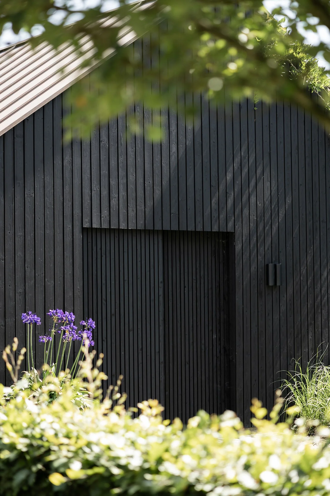 Contemporary black timber barn with a standing seam metal roof and landscaped garden