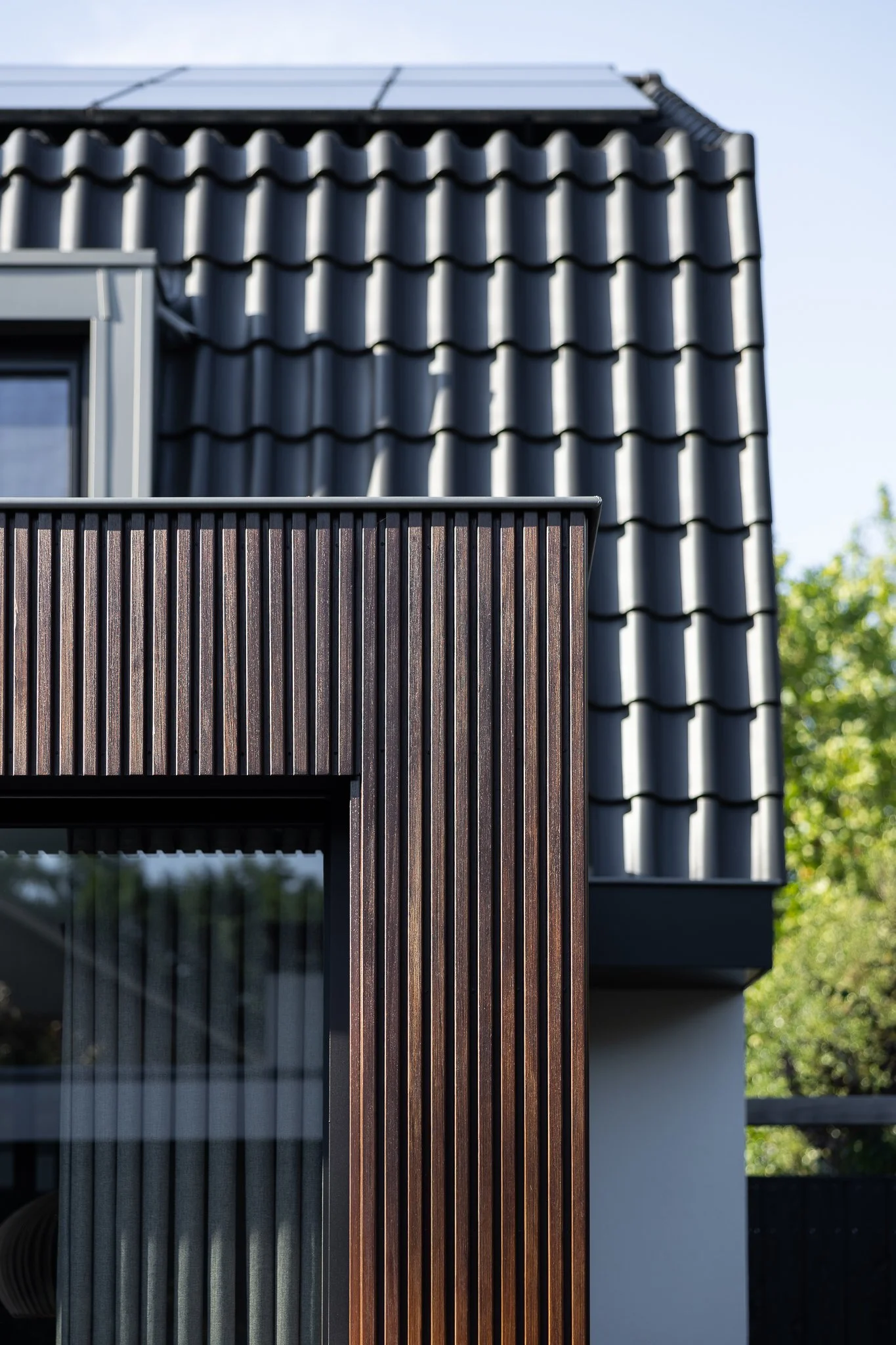 Architectural detail of vertical timber cladding beneath dark roof tiles and solar panels