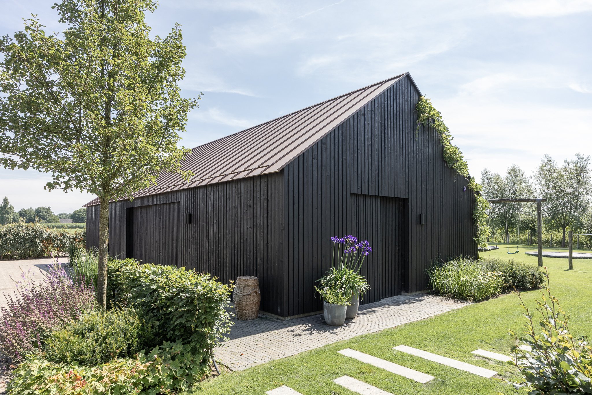 Wide exterior view of a contemporary black timber barn set in a landscaped garden