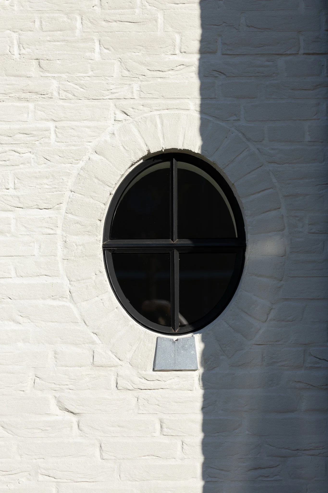 Circular black-framed window set into a textured white brick exterior wall