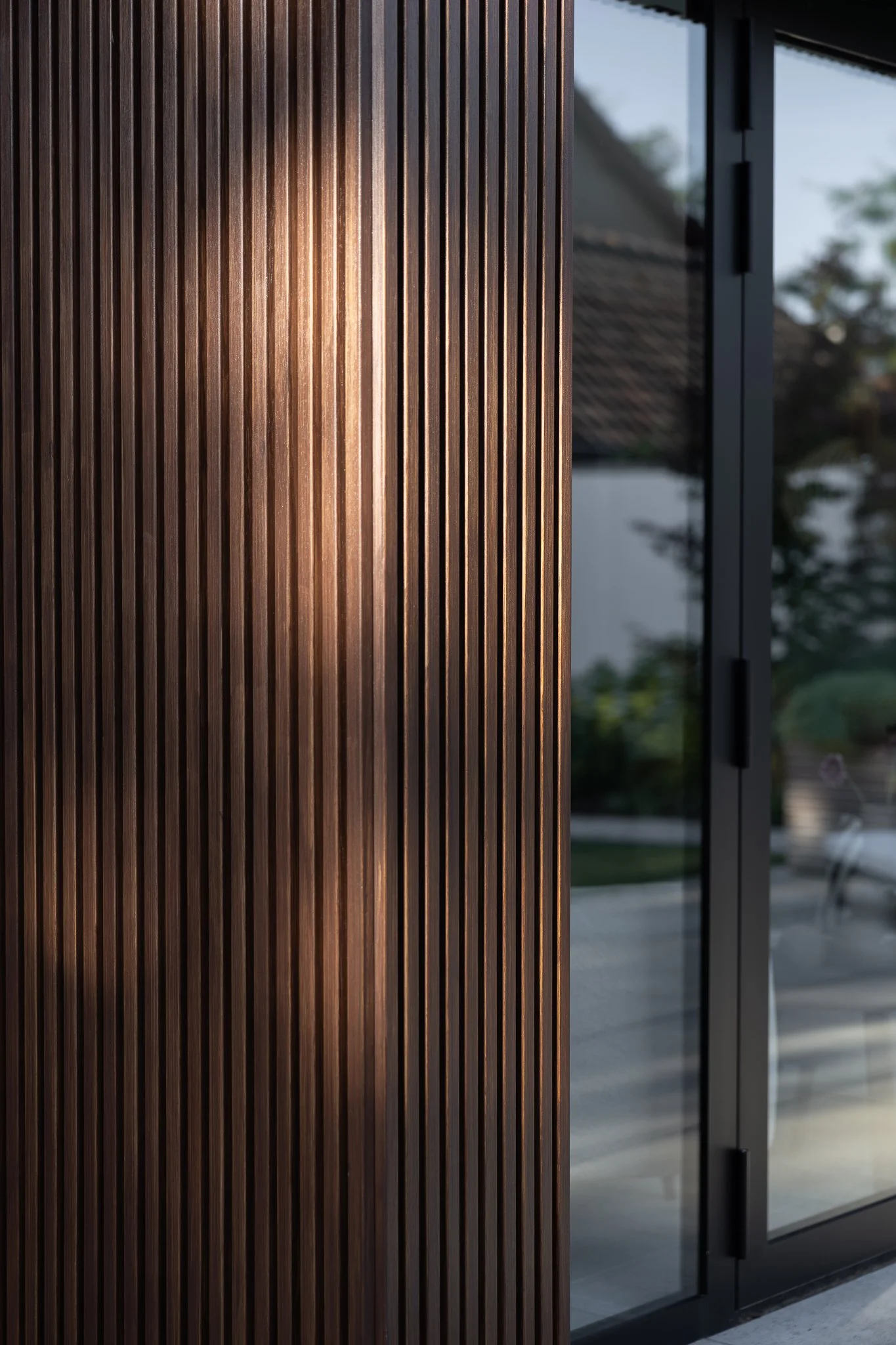 Warm sunlight reflecting on vertical timber cladding beside black-framed glass doors