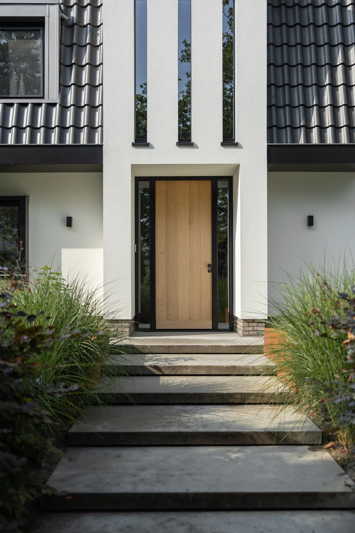 Natural oak front door framed by narrow windows and concrete garden steps