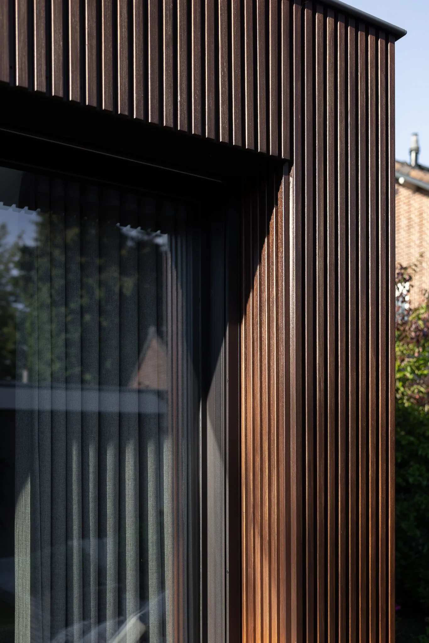 Detailed corner of a timber-clad extension with black-framed glazing and soft sunlight
