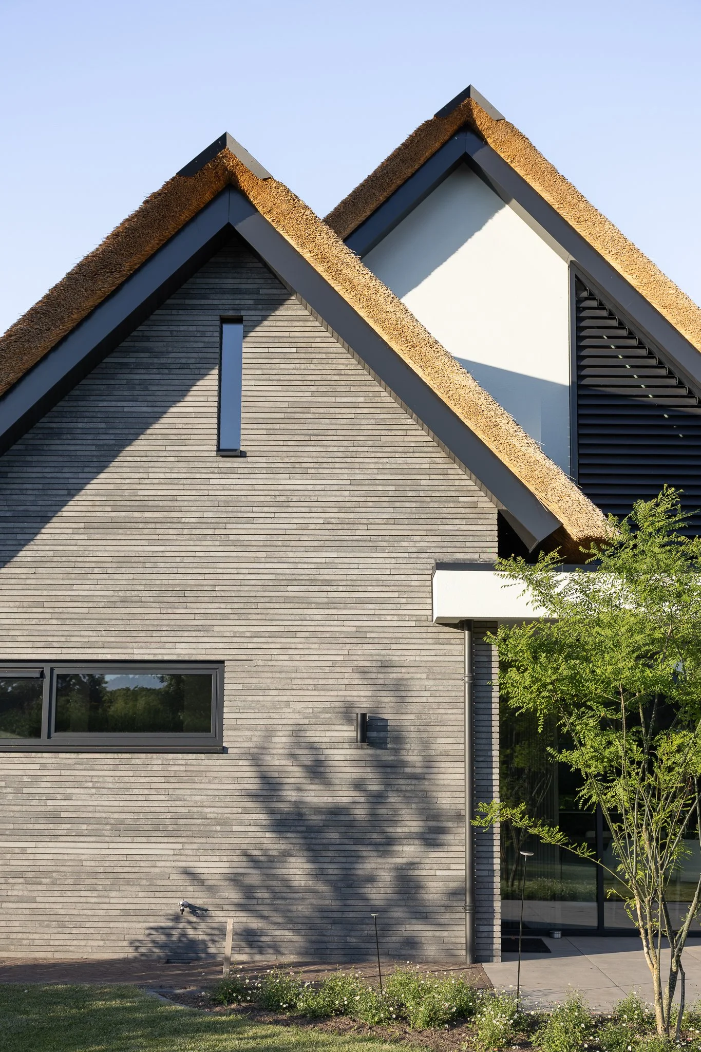 Architectural detail of a thatched roof and grey brick façade framed by green leaves