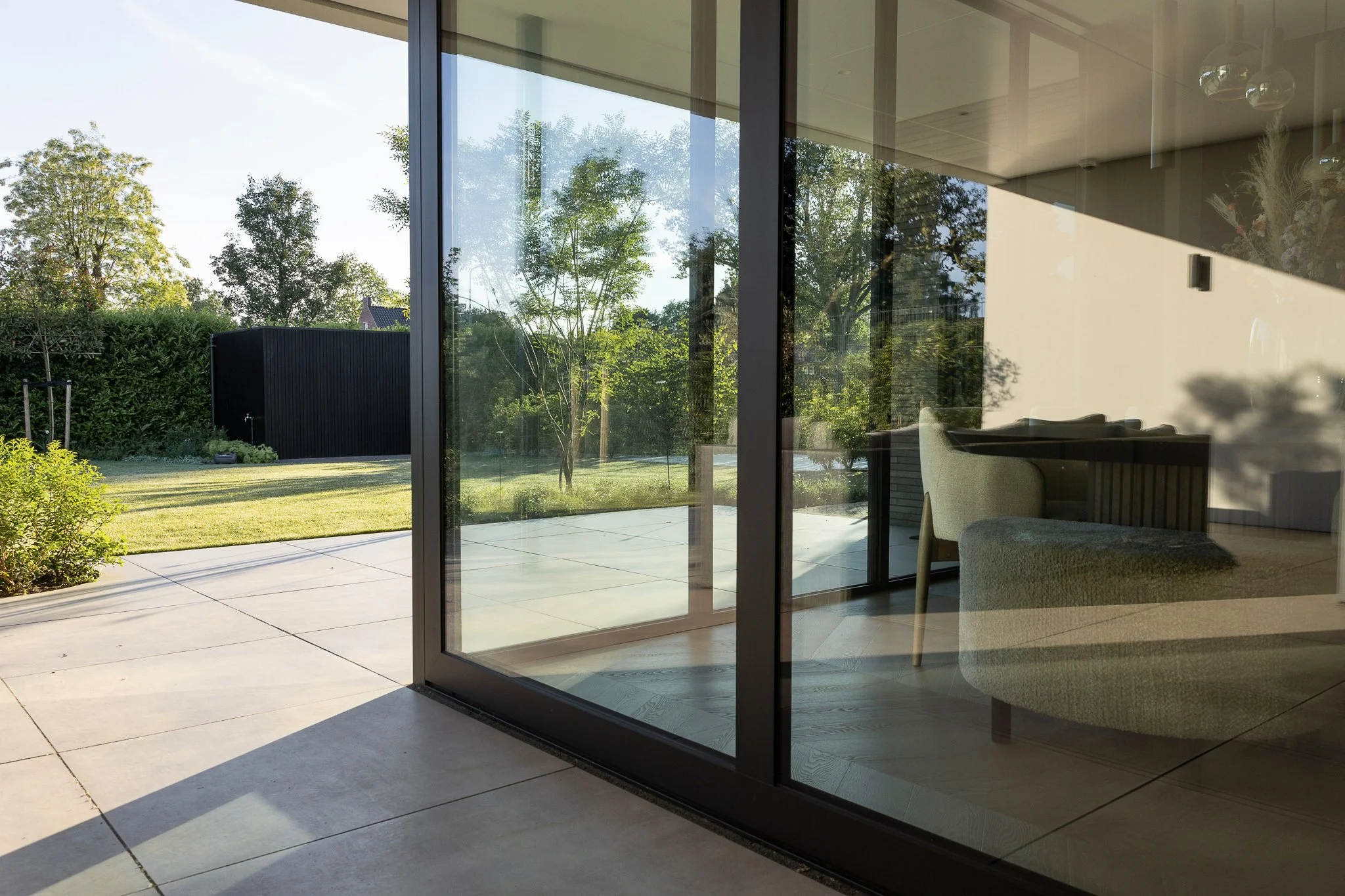 Covered terrace with black steel frames and floor-to-ceiling glass doors overlooking the garden