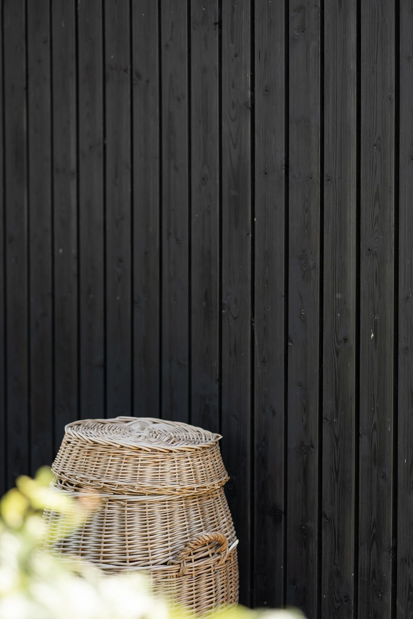 Woven garden baskets against the vertical black timber cladding of a modern barn