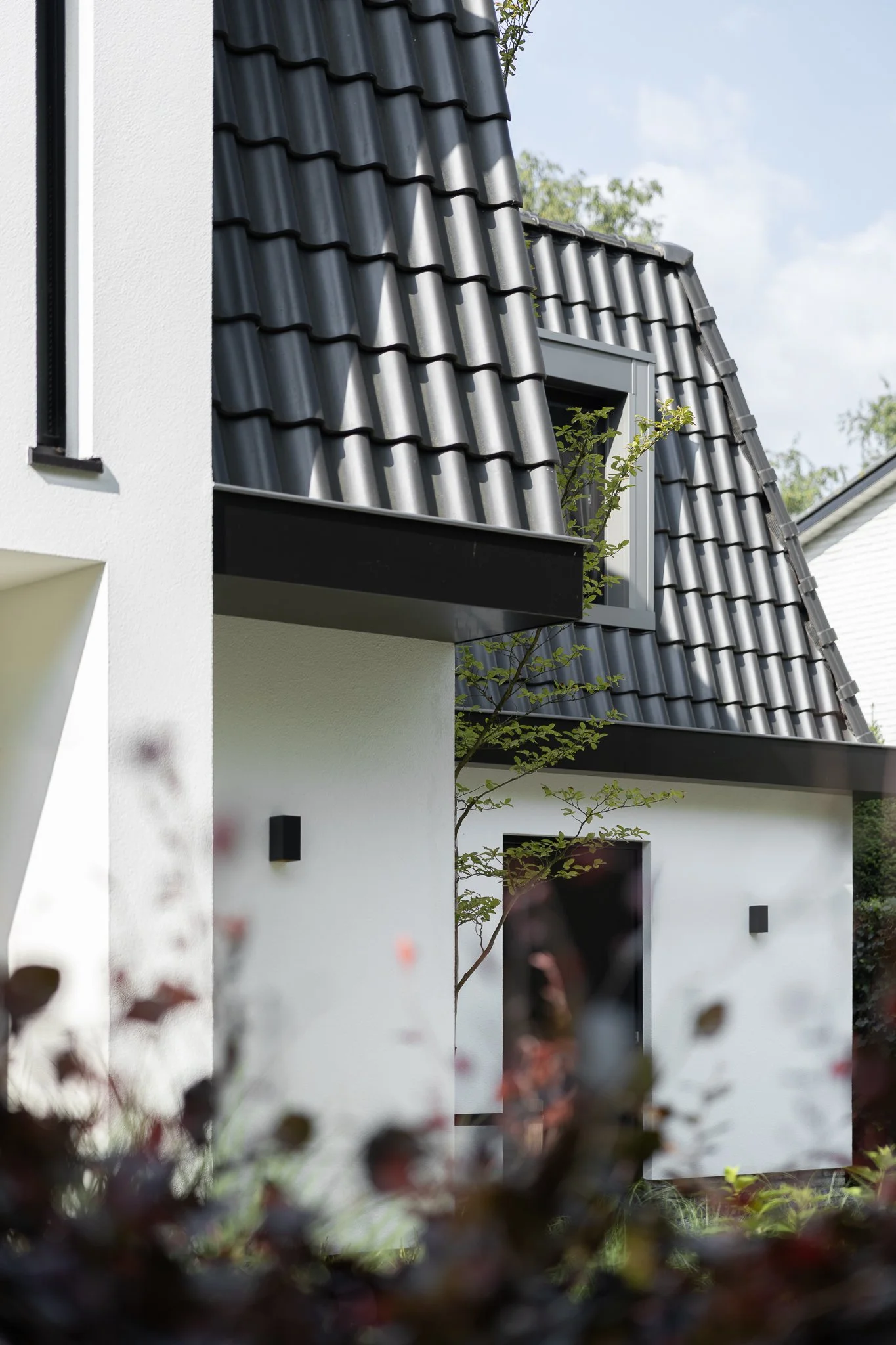Angled exterior view of a modern white villa with dark roof tiles and architectural landscaping