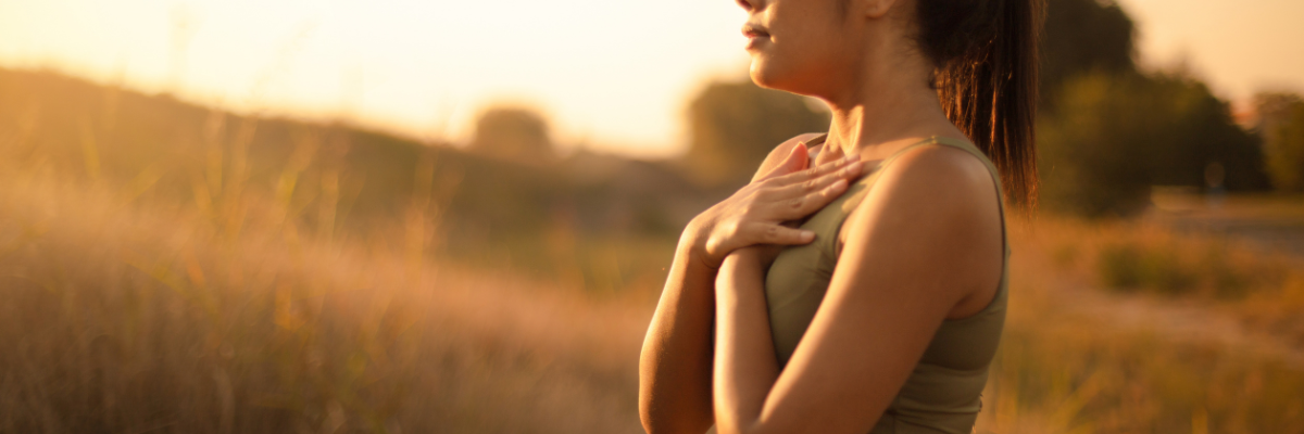 une femme a les deux mains déposées sur le coeur ,qui prend une respiration profonde, une lumière dorée et un champ en arrière plan