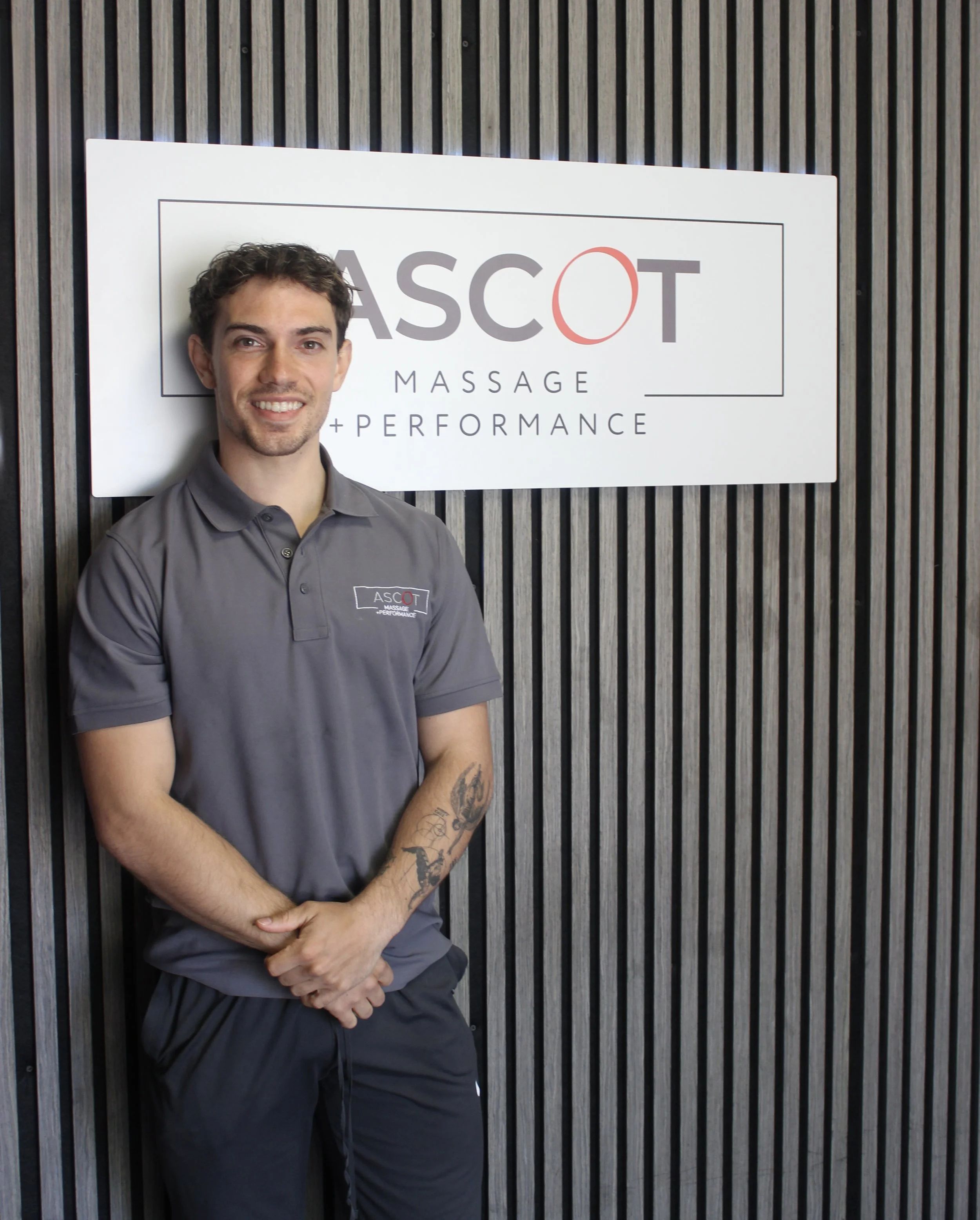 Sam standing in front of his ascot massage and performance logo