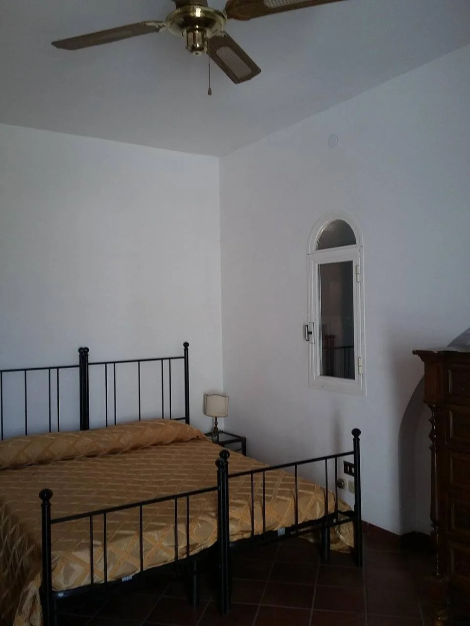 Camera da letto con letto in ferro battuto, un comodino con lampada e una finestra con arco.