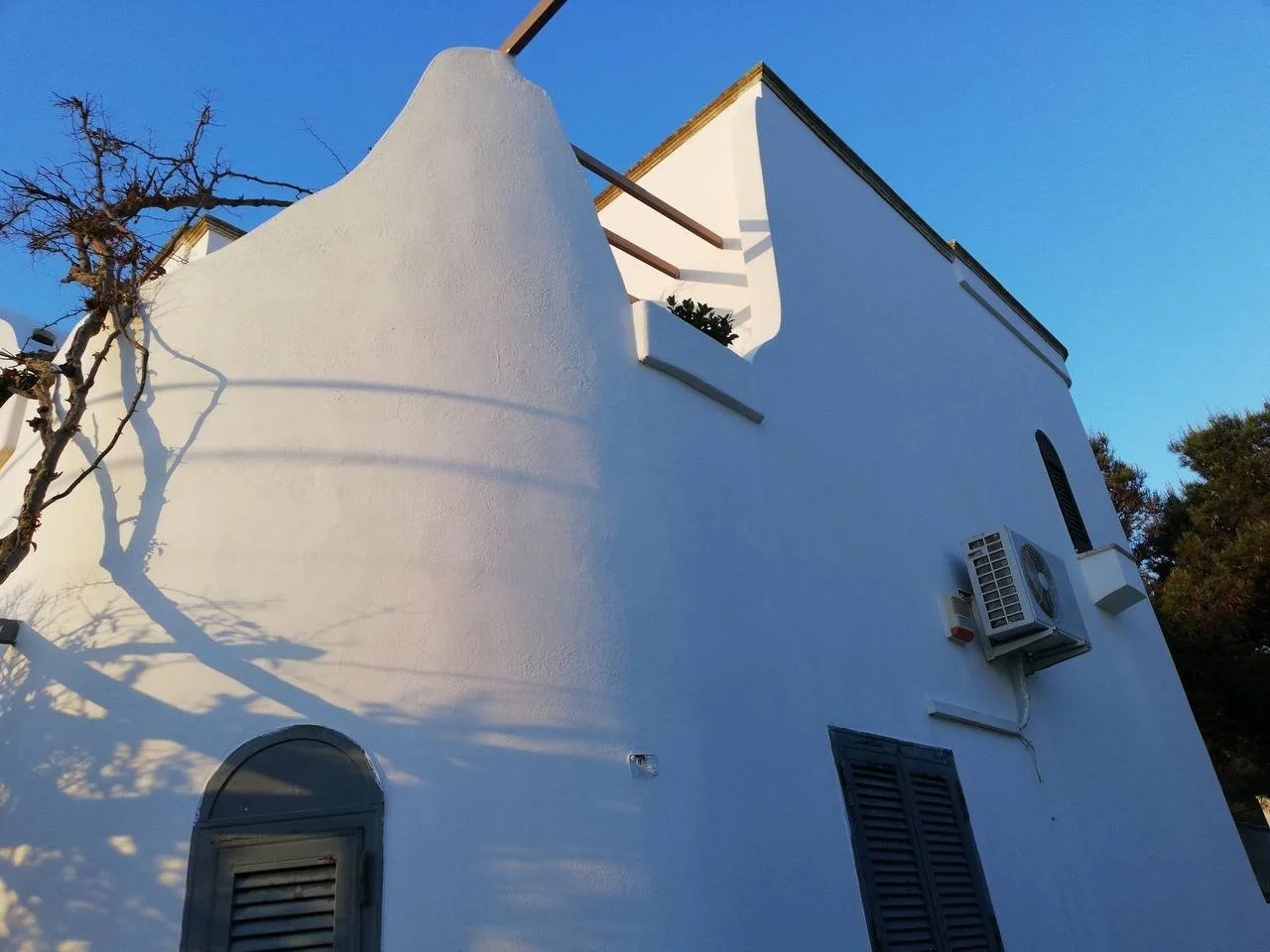 Edificio bianco con parasole, aria condizionata, e finestra con tapparella, sotto un cielo blu