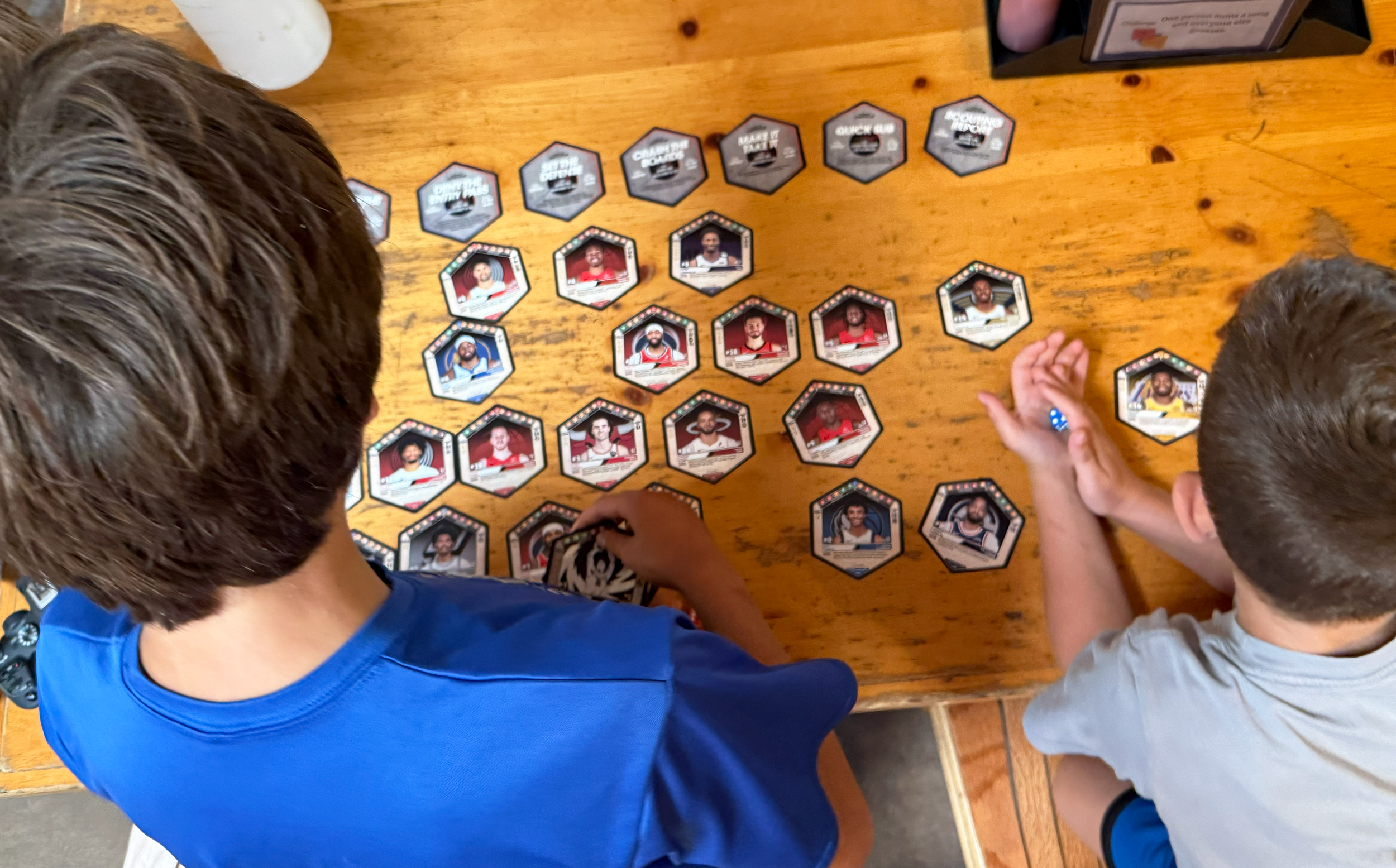 Two children playing a tabletop basketball game with cards of NBA basketball players on a wooden table.