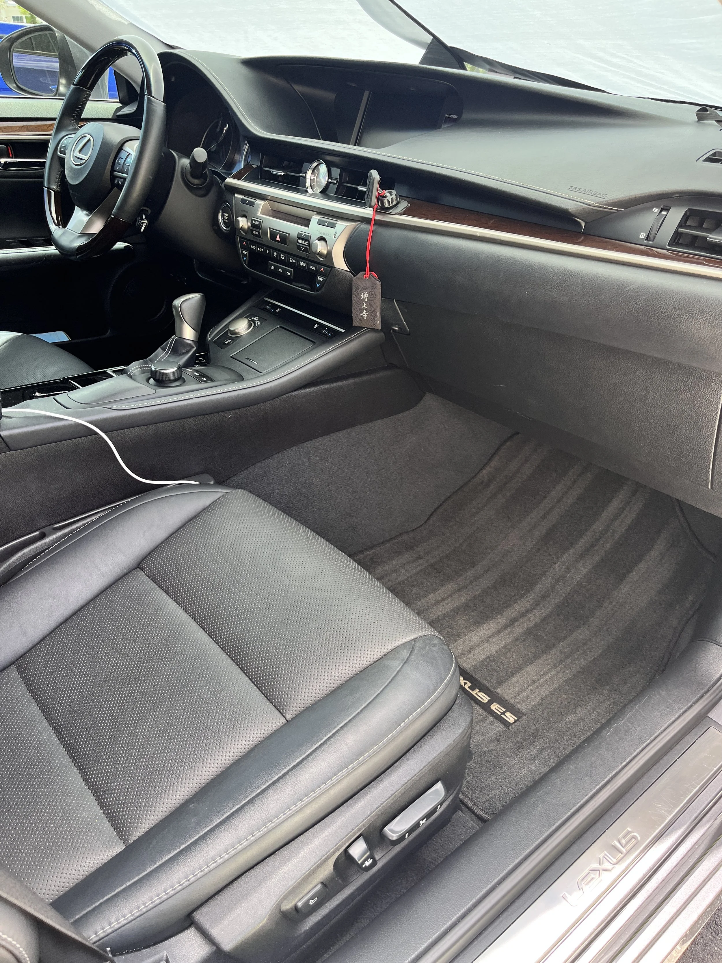 Interior of a luxury Lexus vehicle, showing the driver's seat, steering wheel, dashboard, center console with controls, and front passenger footwell with a Lexus-branded floor mat.