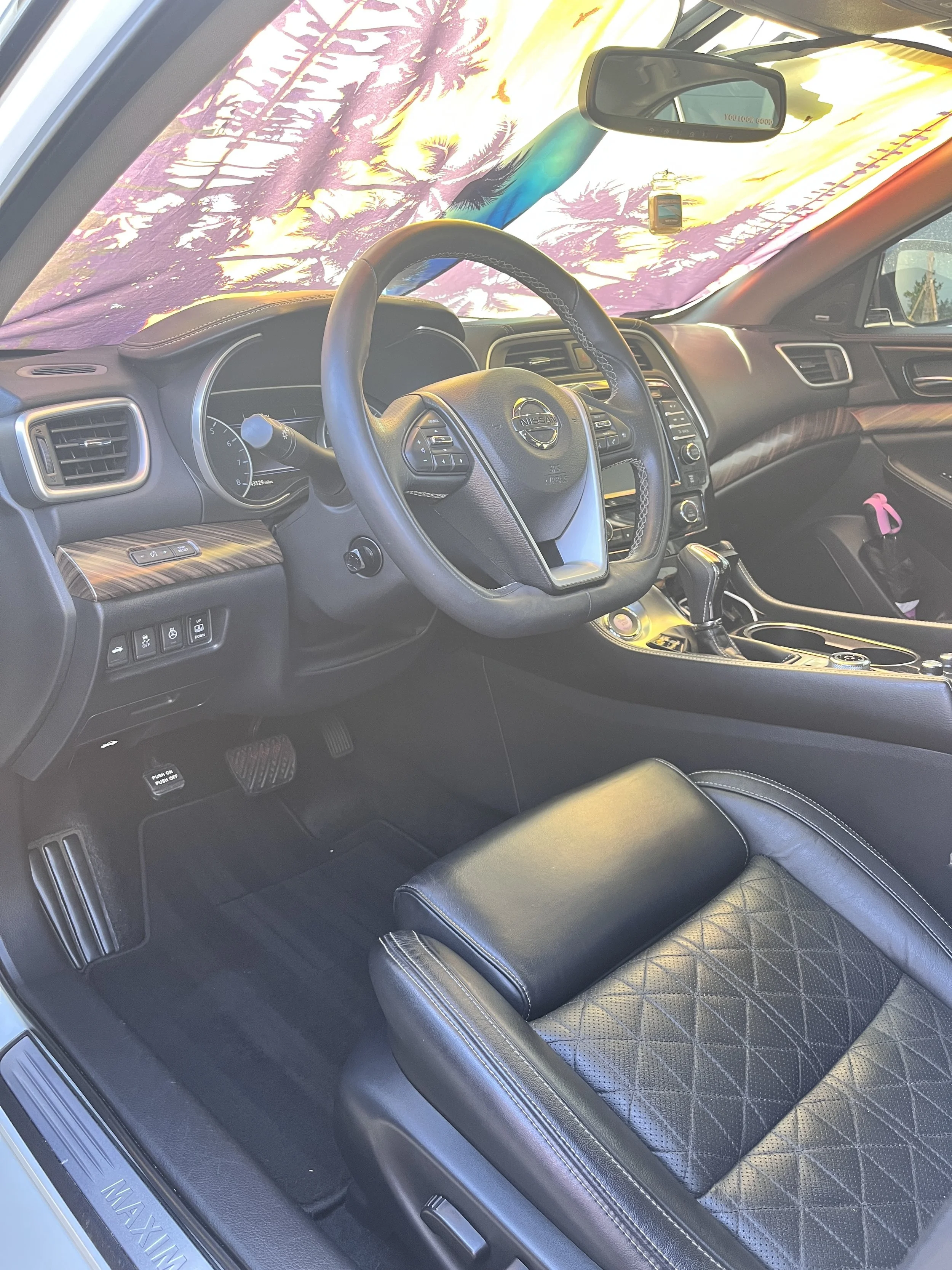 Interior of a Nissan Maxima car showing the steering wheel, dashboard, and front passenger seat with a leather seat cover.