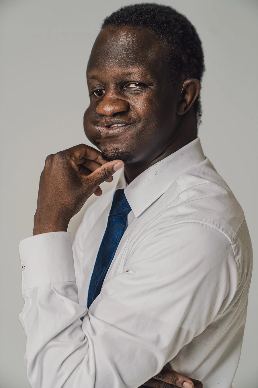 A man in a white shirt and blue tie posing with his hand on his chin, looking thoughtfully at the camera.