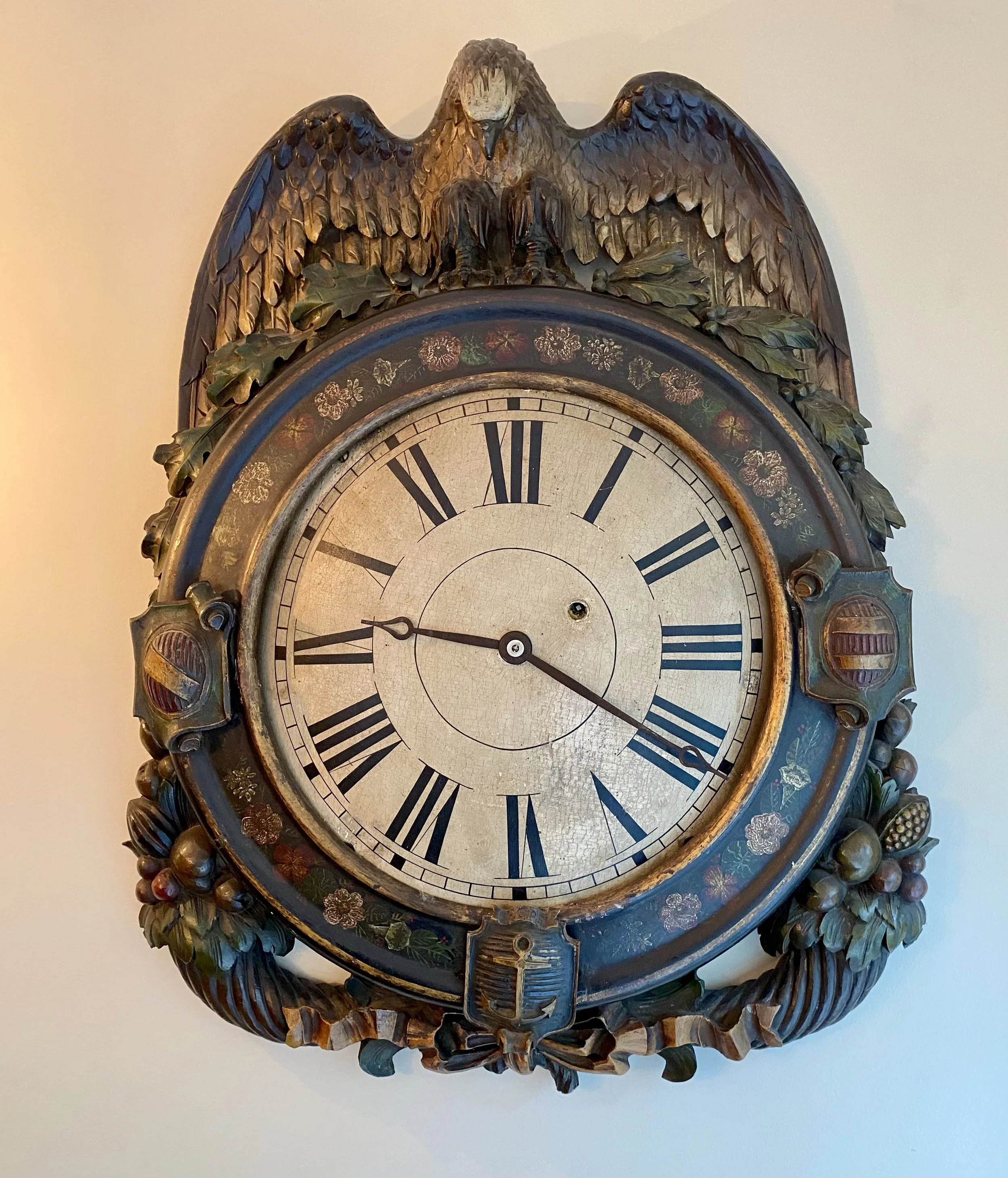 Regency carved wood polychrome painted wall clock case, early 19th century,
The crest carved with a perched polychromed eagle over a berry and leafage motif centering on a circular flower painted case with carved cabochons centering original wood pai