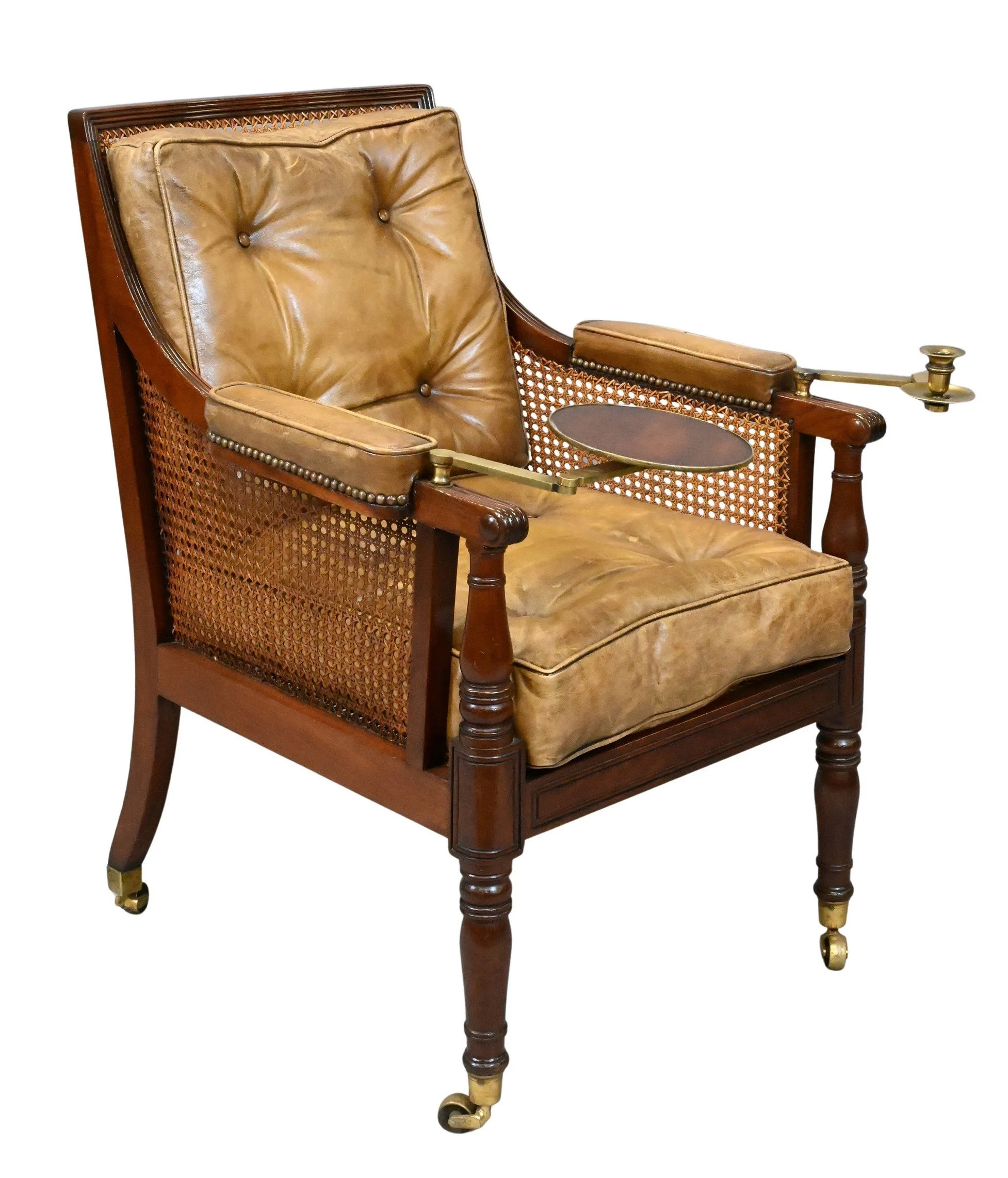 English Regency Caned Library Chair
having removable brass-mounted candle stand and circular wood tray, the chair with caned seat, back, and sides, fitted with later tufted brown leather cushions, raised on turned baluster legs ending in brass caster