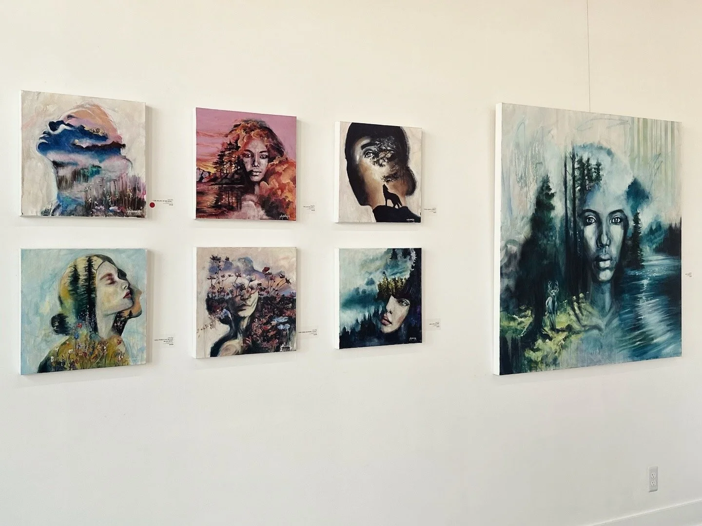 Display of eight colorful paintings in an art gallery, featuring portraits and nature scenes with a mix of realistic and abstract styles.