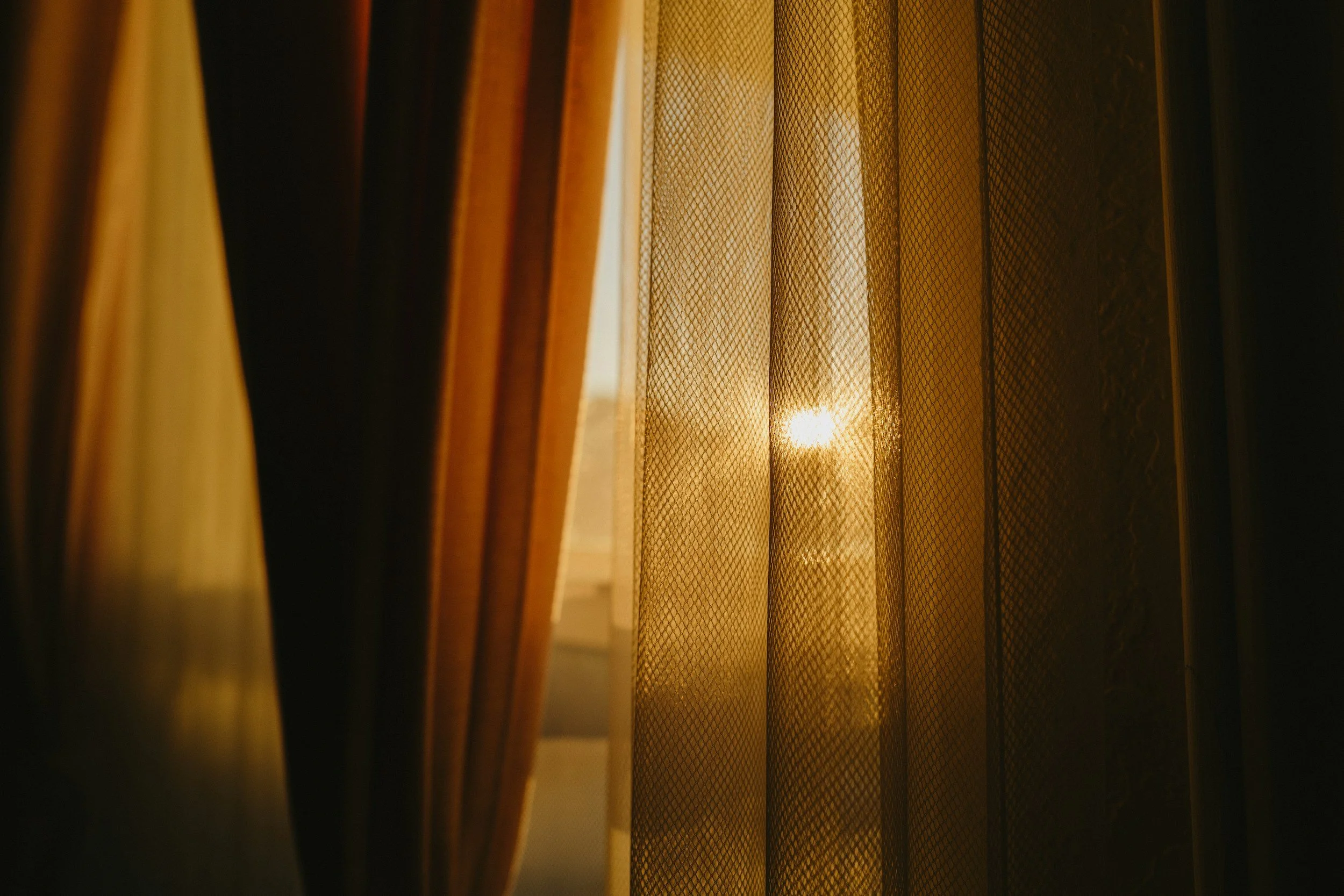 Sunlight shining through a sheer, patterned curtain in a warmly lit room.