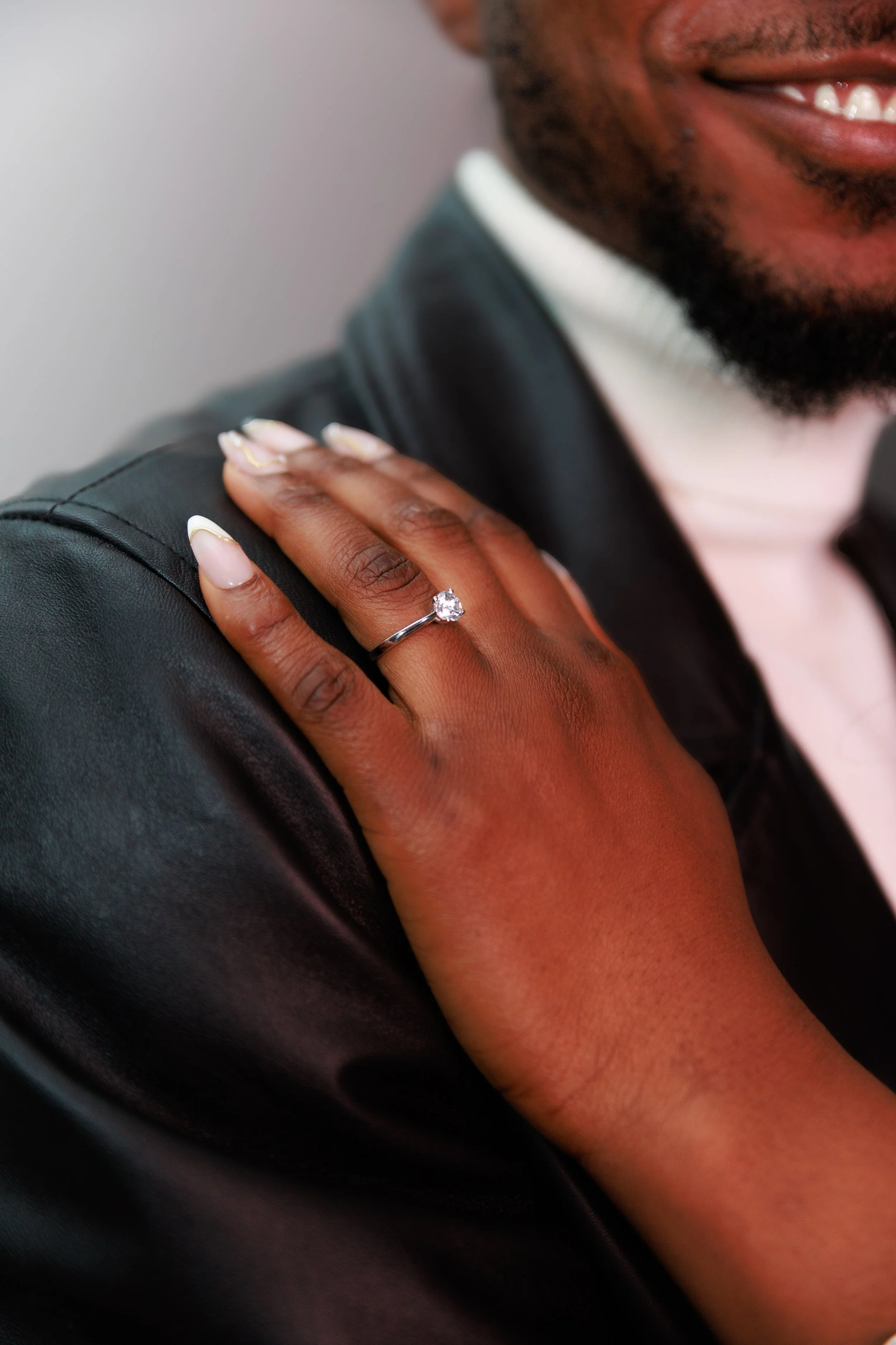 A couple dressed in traditional African attire, featuring coral bead necklaces and headpieces, standing outdoors against a green leafy background, smiling at the camera.
