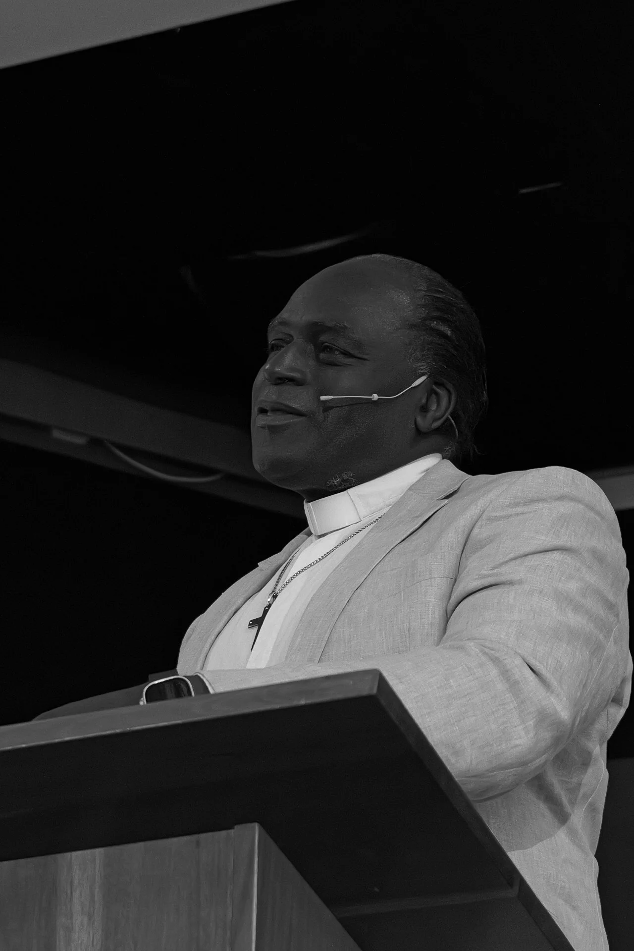 Two women smiling and sitting close together at a social event with purple lighting, one in a pink dress with braids and the other in a black dress with jewelry.