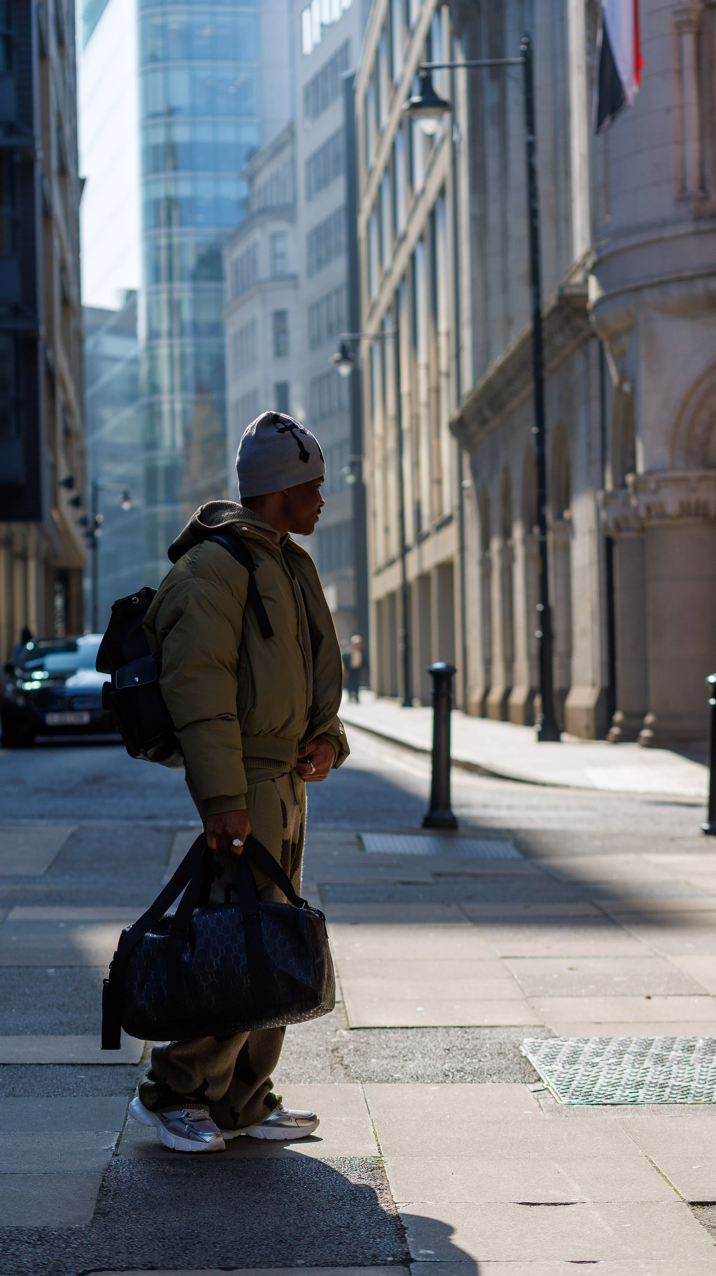 A woman with long, styled hair and wearing a detailed, elegant dress is sitting on a teal chair in front of a white wall with a window showing a cloudy sky outside.