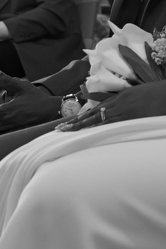 A woman in a black strapless dress at a celebration, smiling and posing with her hand near her face in a peace sign, with a decorated event space with purple lighting in the background.