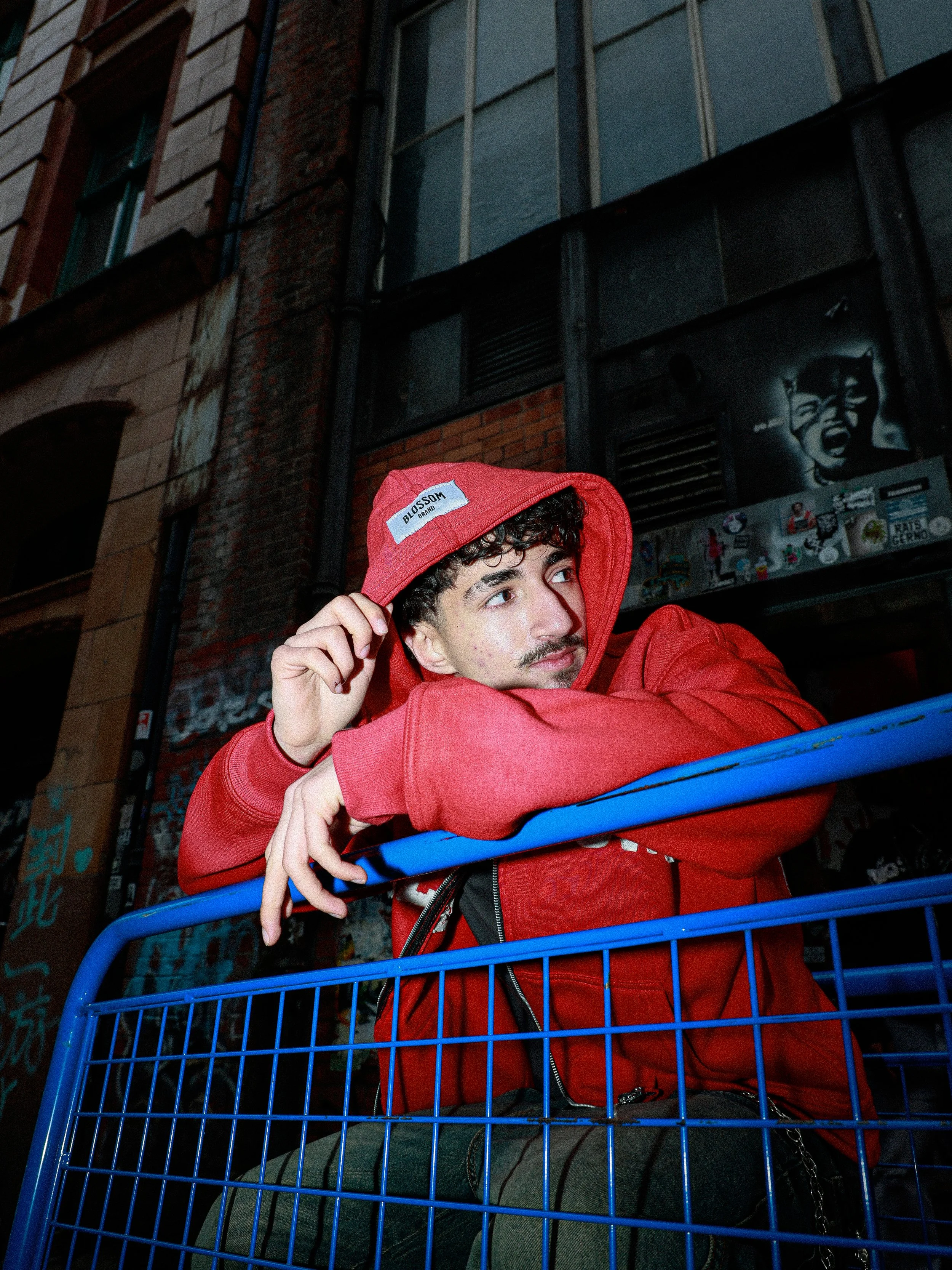 A young man singing and playing guitar on stage, with eyes closed, in front of a red and black background with a plant on the right side.
