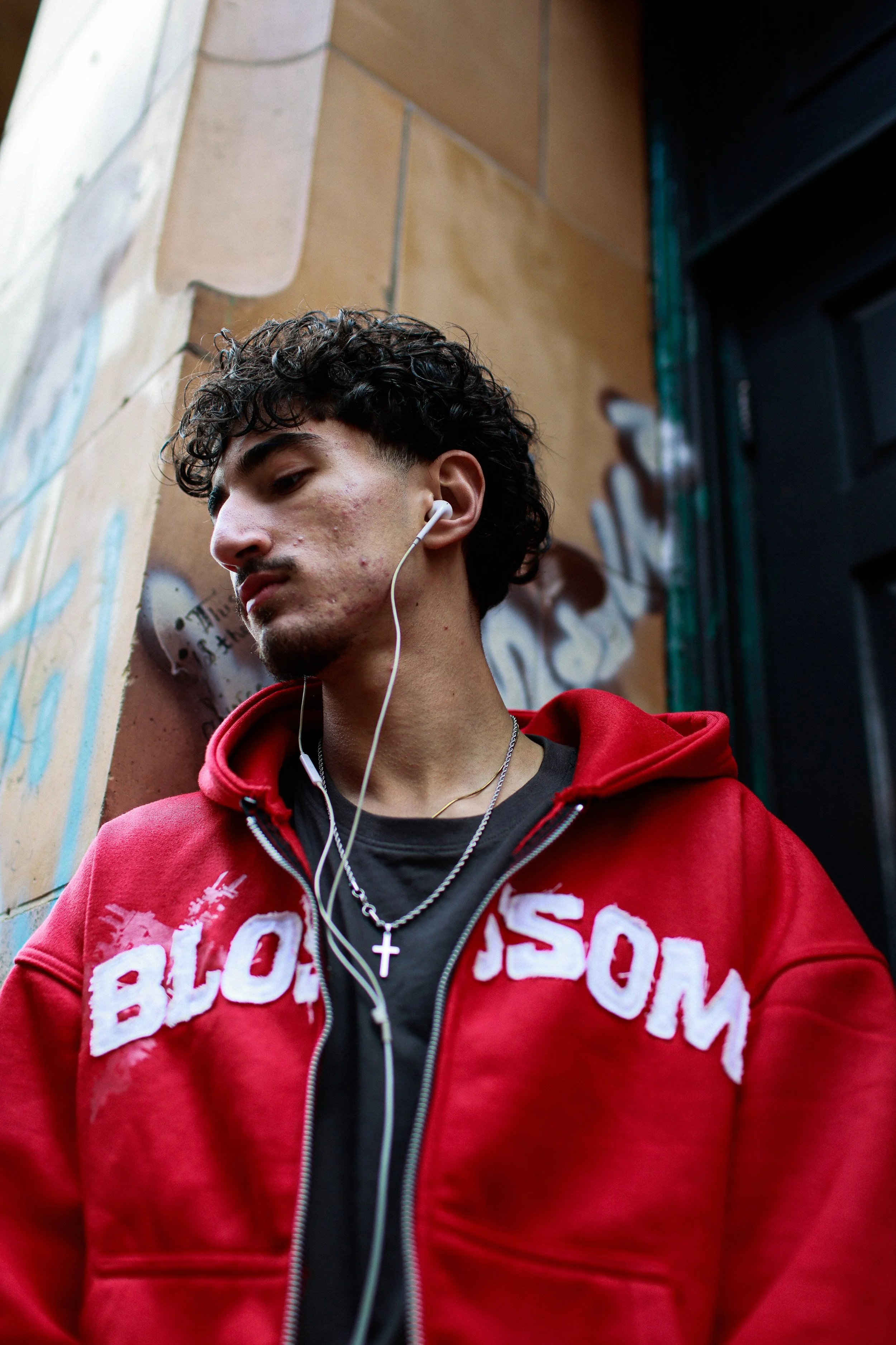 A young man playing an electric guitar on stage, with dark blue and black backdrop, and a drummer partially visible behind him.