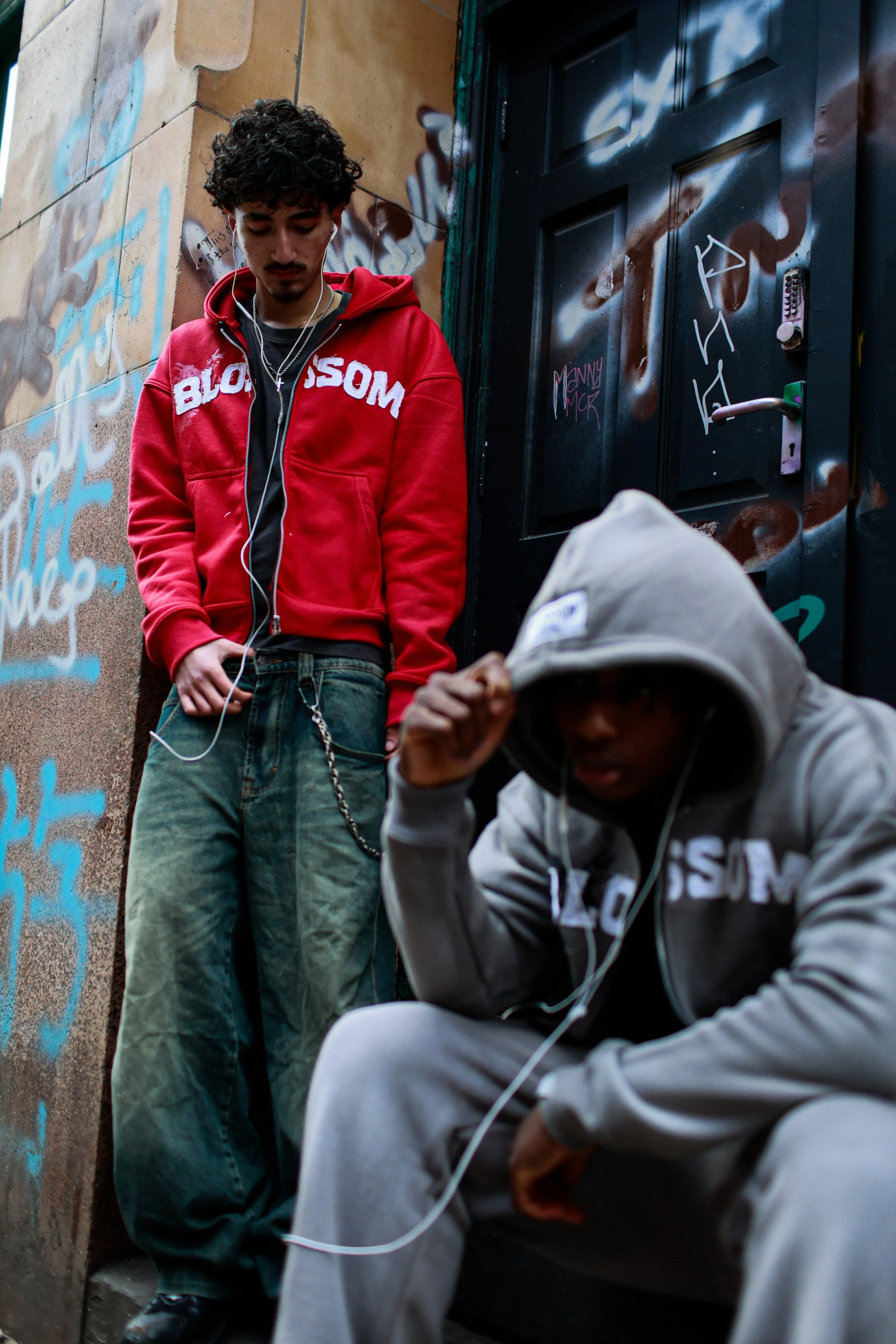 A young woman with wavy blonde hair singing into a microphone on stage, wearing a black, sparkly dress, with another person playing keyboard in the background.