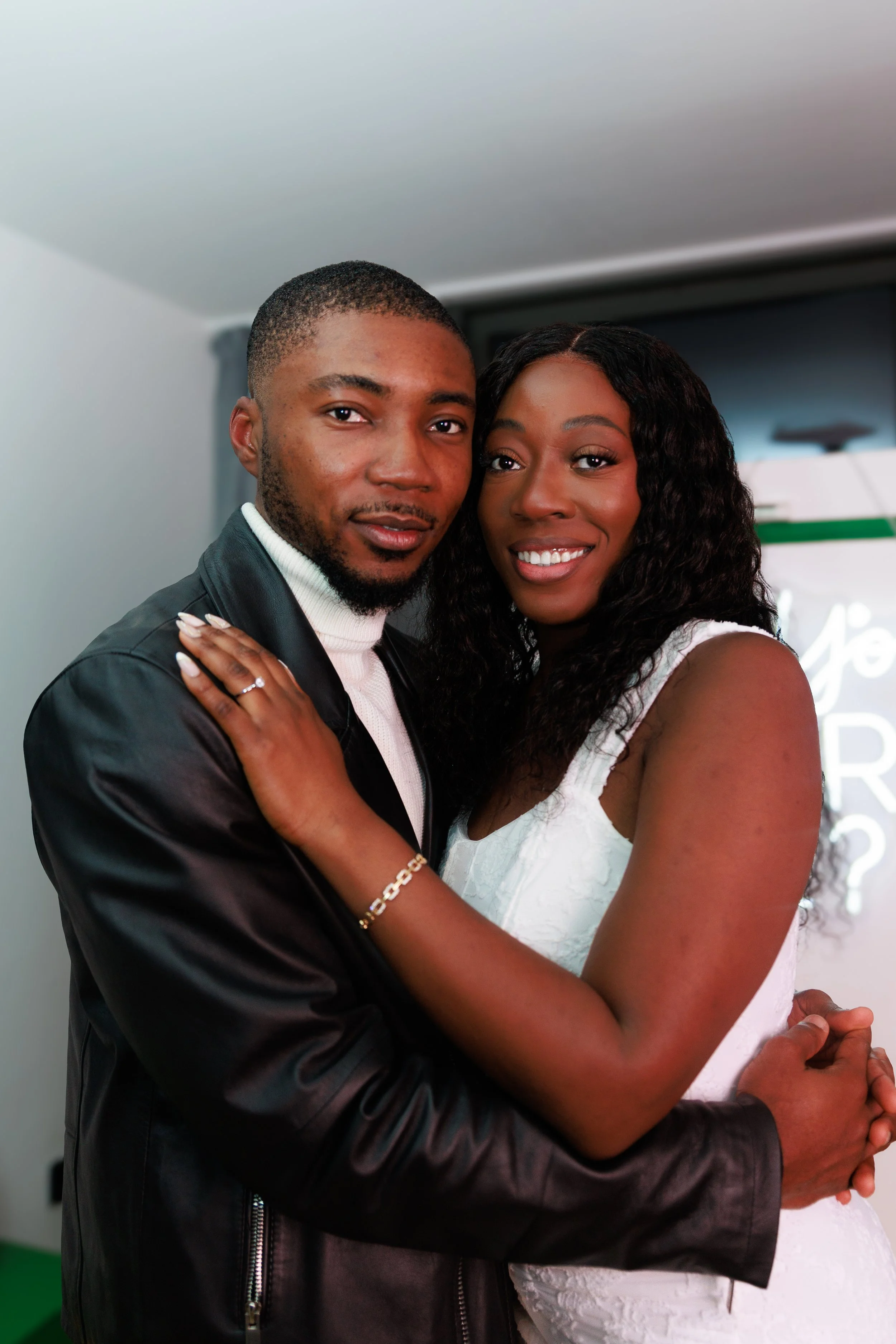 A woman wearing traditional African attire with a red beaded headwrap and gold decorative ornaments, with her face partially obscured by a red feathered accessory, against a green leafy background.