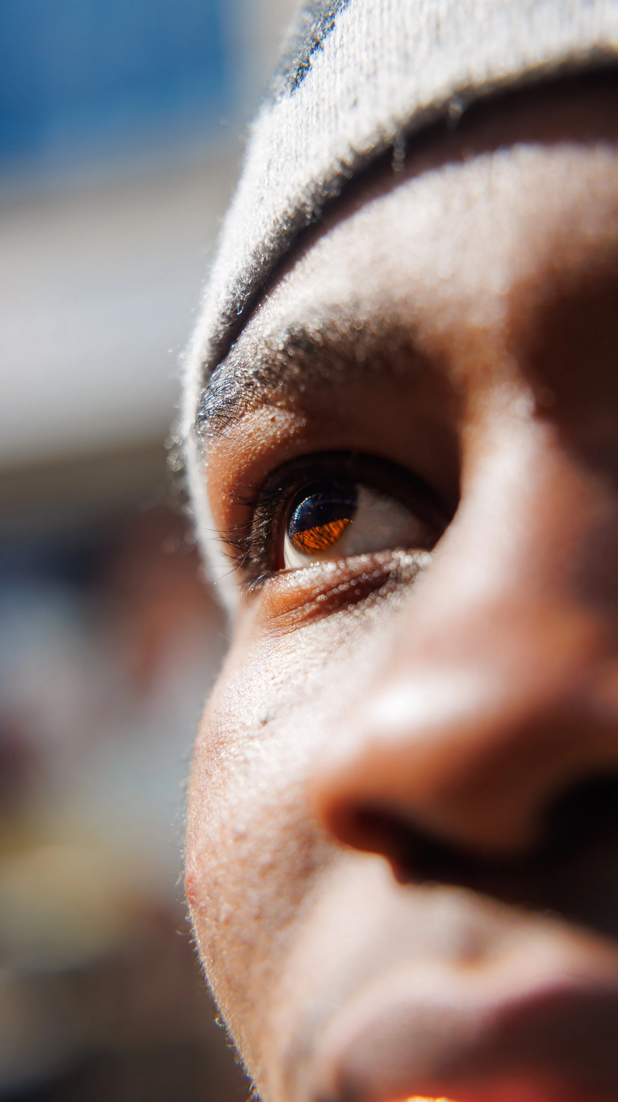 Two women smiling and looking at each other, wearing matching cream-colored dresses with gold sequins, standing against a brown background.