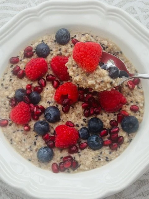 Bowl of oatmeal topped with fresh raspberries, blueberries, and pomegranate seeds, with a spoon lifting a portion.