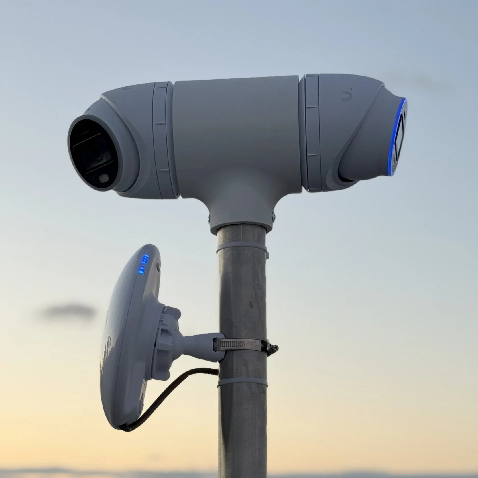 A public electric vehicle charging station with two charging units mounted on a pole against a sunset sky.