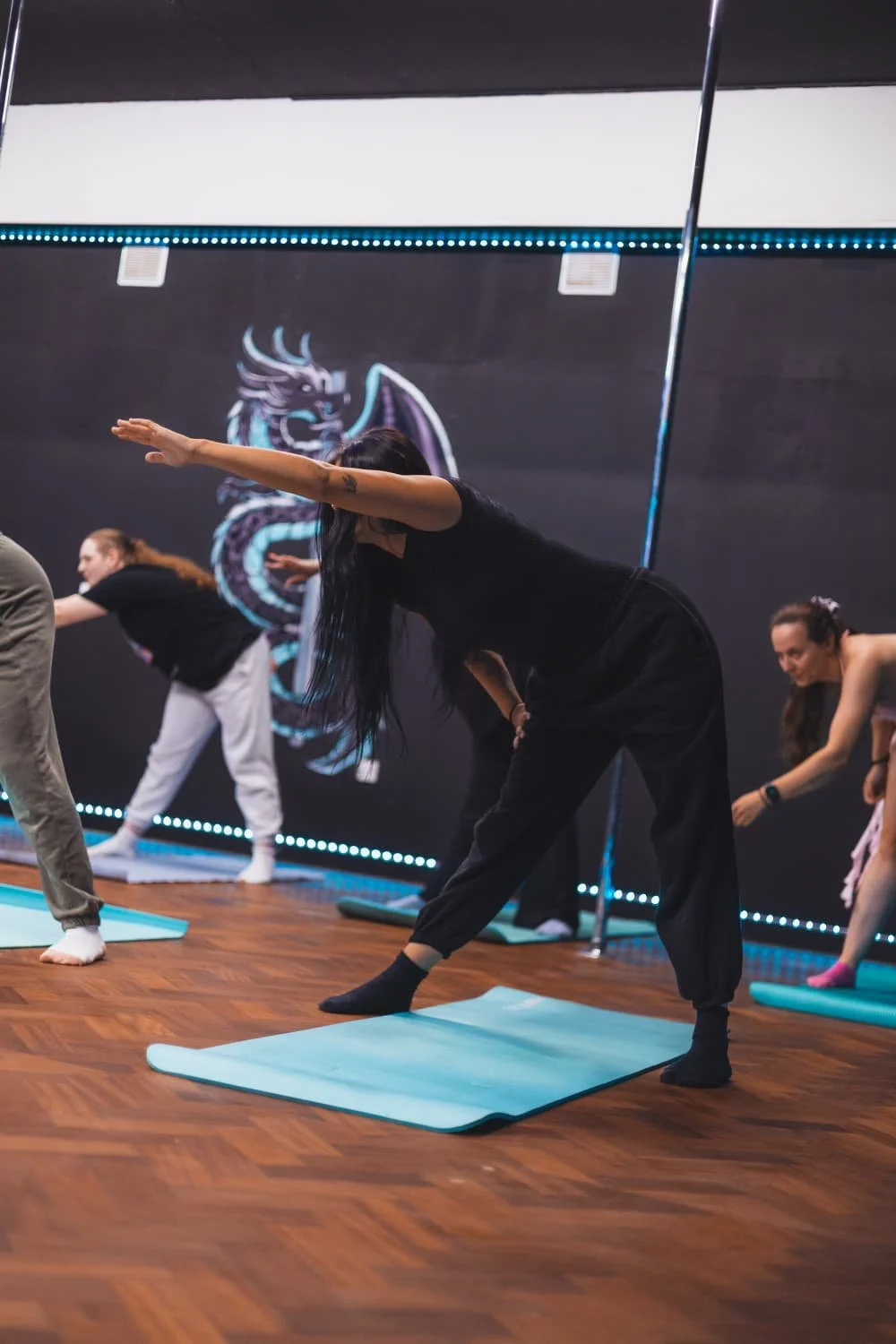 People participating in a yoga class on mats, stretching their arms and bodies in a studio with a dragon mural on the wall.