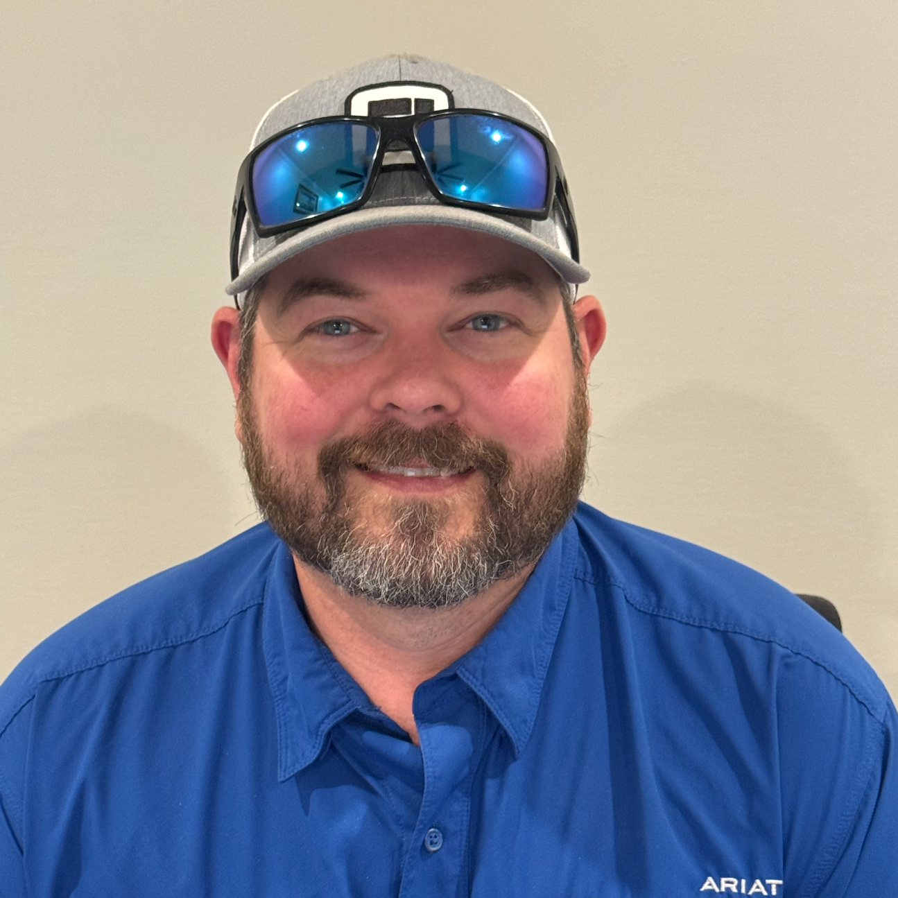 man wearing a baseball cap with sunglasses on top and a blue shirt, smiling indoors