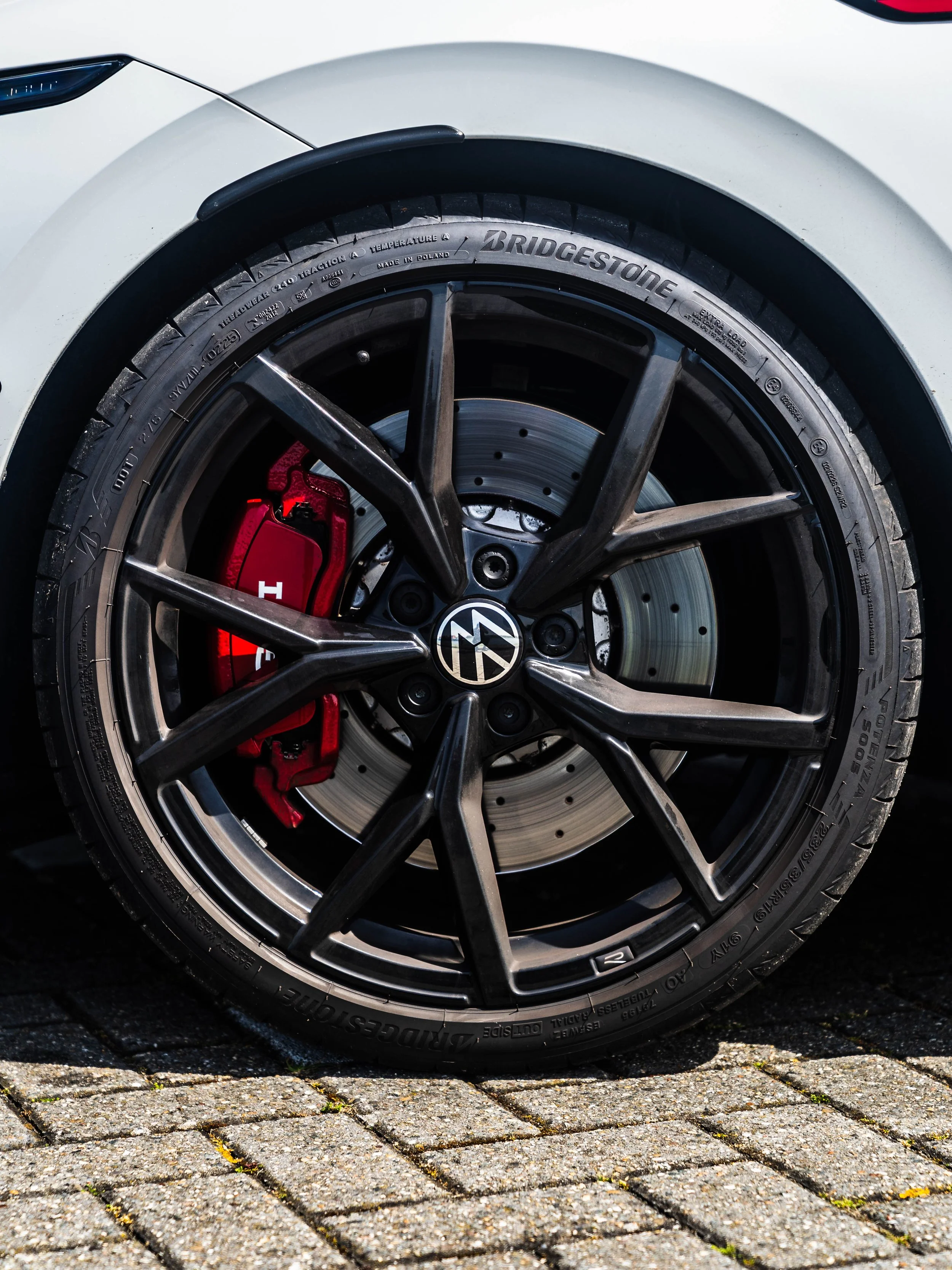Close-up van een auto wiel met velg en remklauw, merk Volkswagen, op een stenen weg. Tante remklauw is rood.