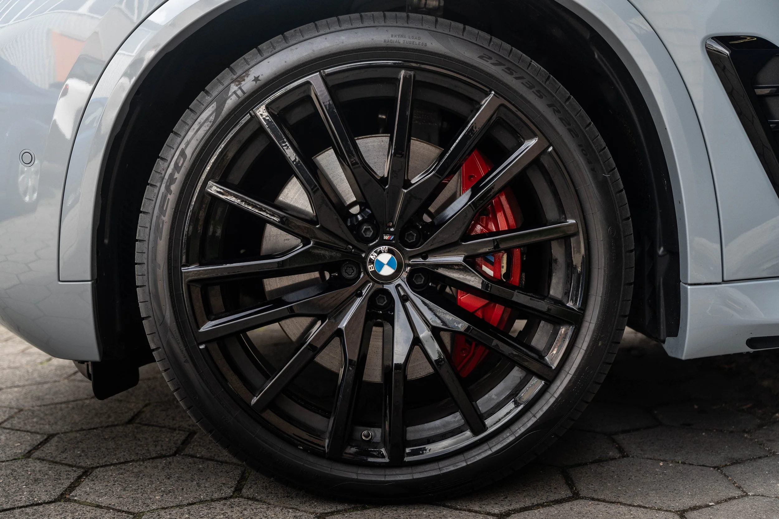 Close-up van het voorwiel van een BMW auto, met zwart velg, rode remklauw en een band met de specificaties 275/35 ZR 22.