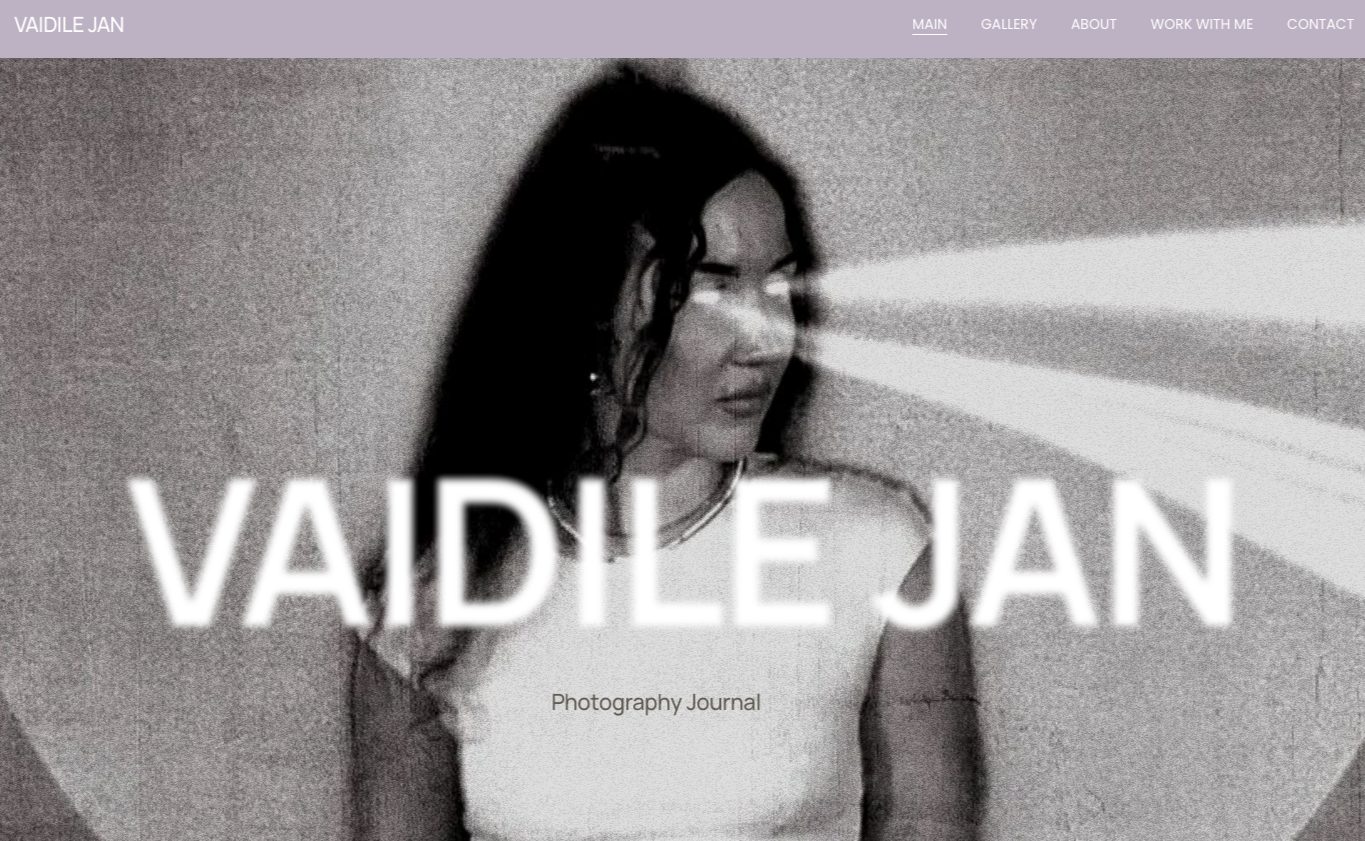 Black and white photo of a woman with long dark hair, standing against a plain wall, with light beams shining on her face. The text 'VAIDLE JAN Photography Journal' is overlaid on the image.
