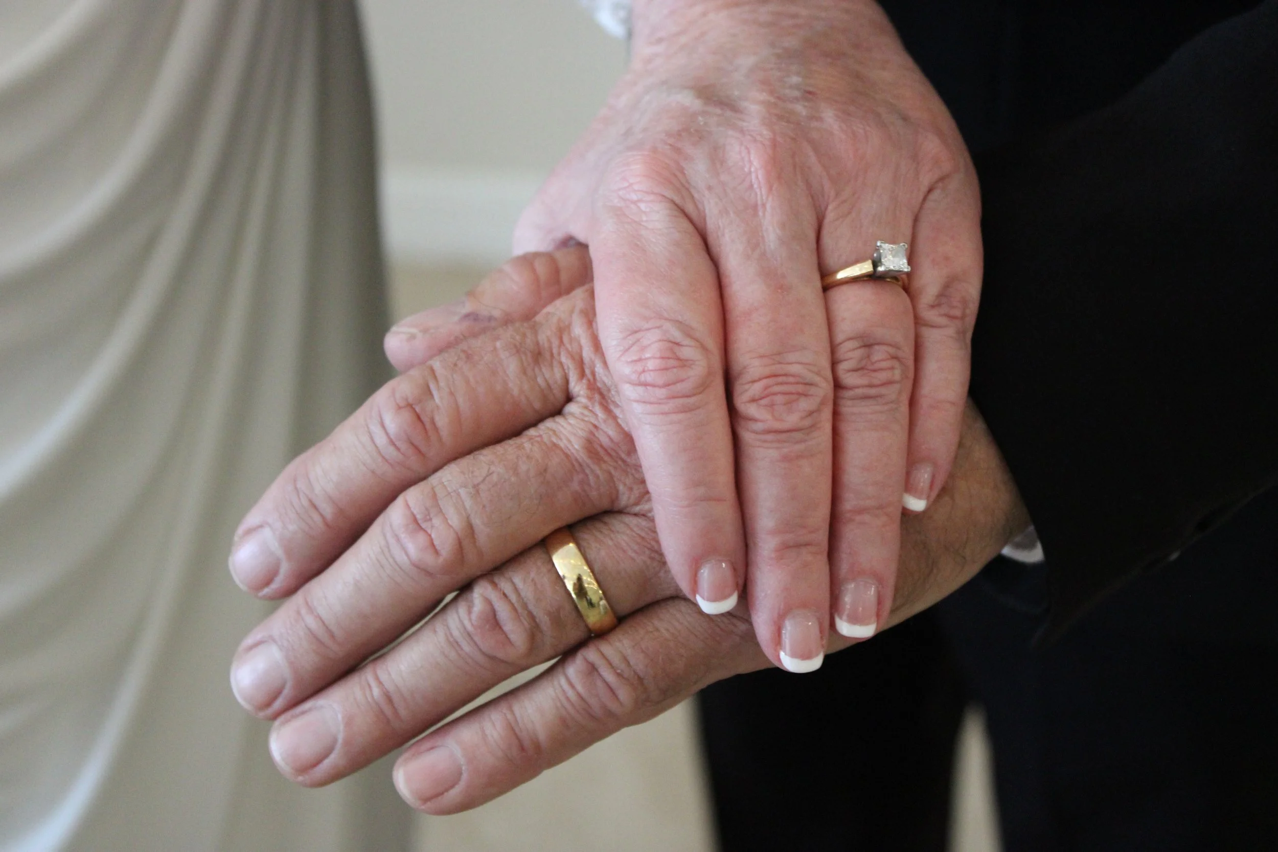 Close-up of a couple holding hands, showing wedding rings on their ring fingers.