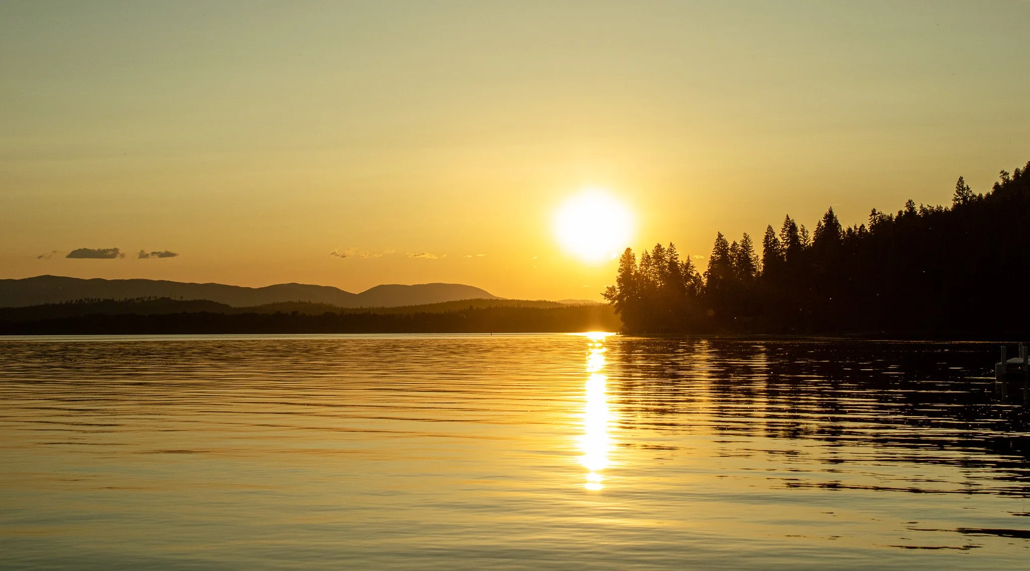 Sun setting over a calm lake with silhouetted trees and distant mountains